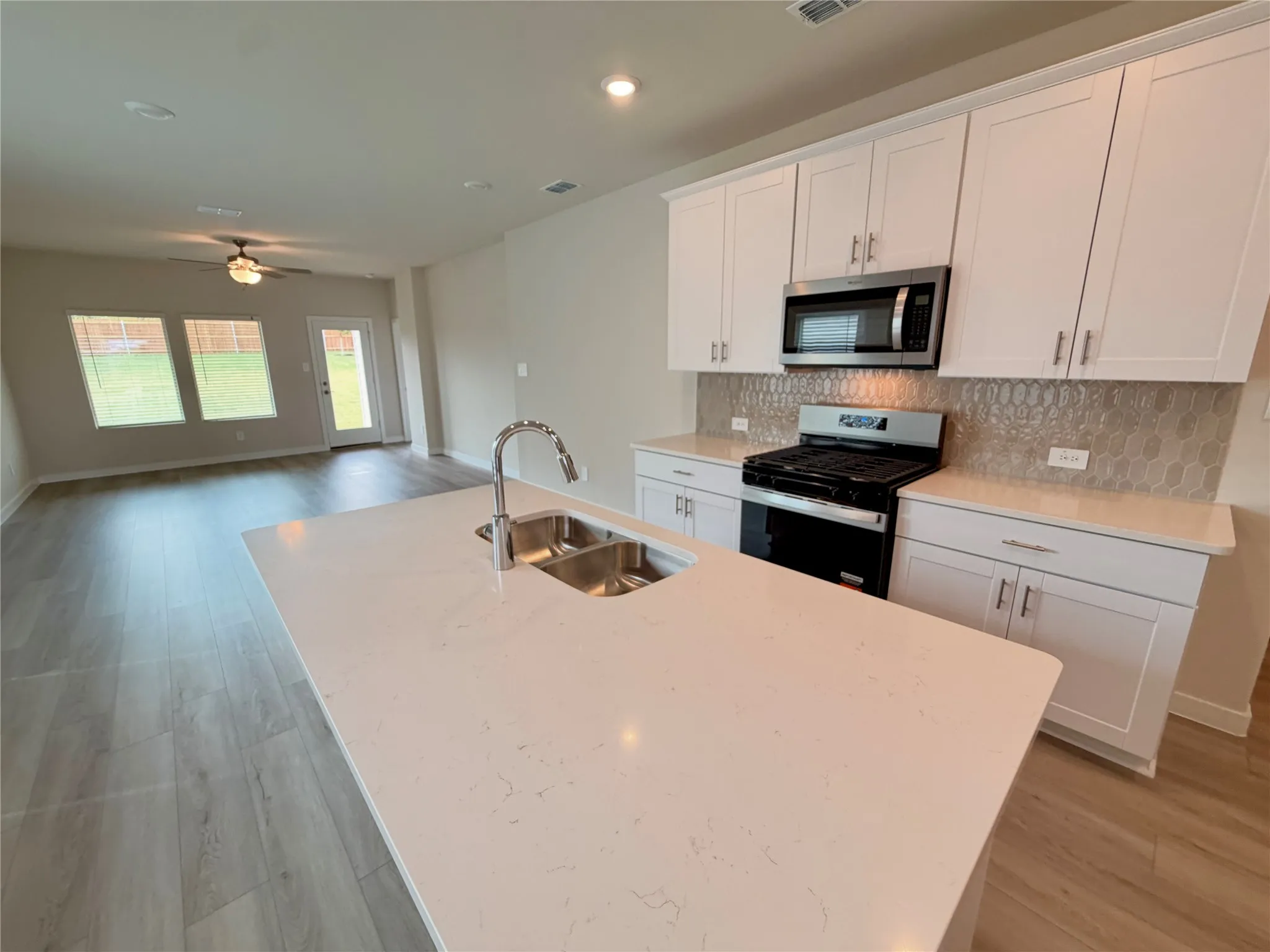 Kitchen featuring a central island with a quartz countertop and stainless steel undermount sink, shaker-style cabinetry, patterned tile backsplash, and recessed lighting