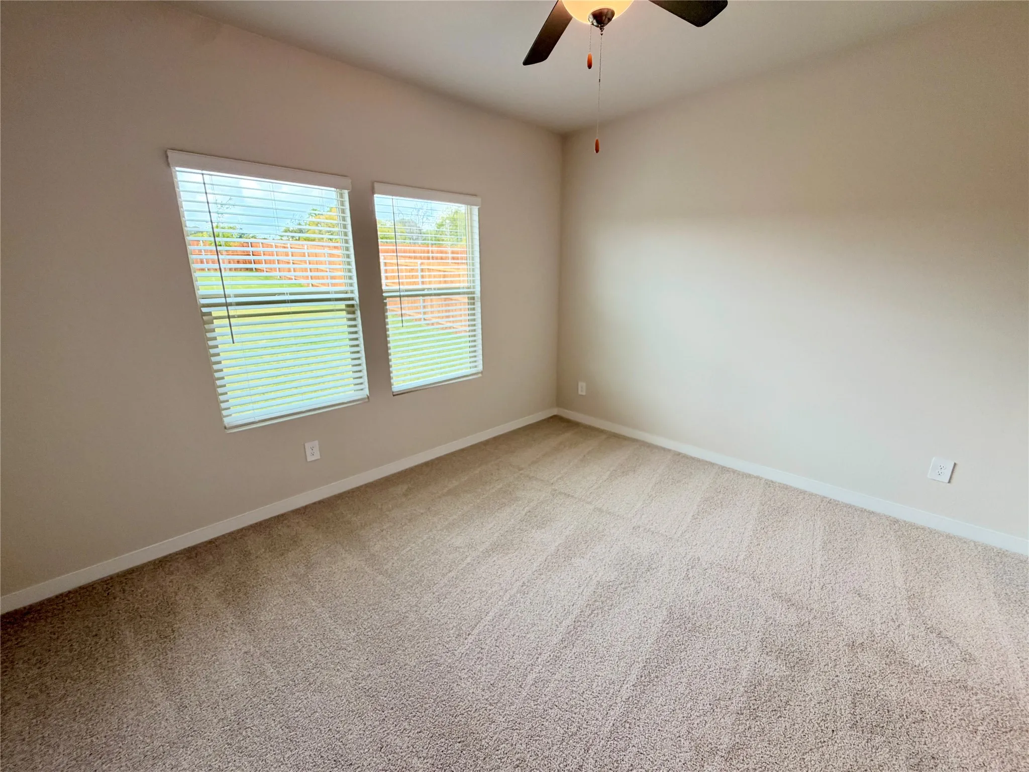 Neutral-toned interior featuring wall-to-wall carpeting, dual windows with integrated blinds, and a ceiling-mounted fan with light fixture