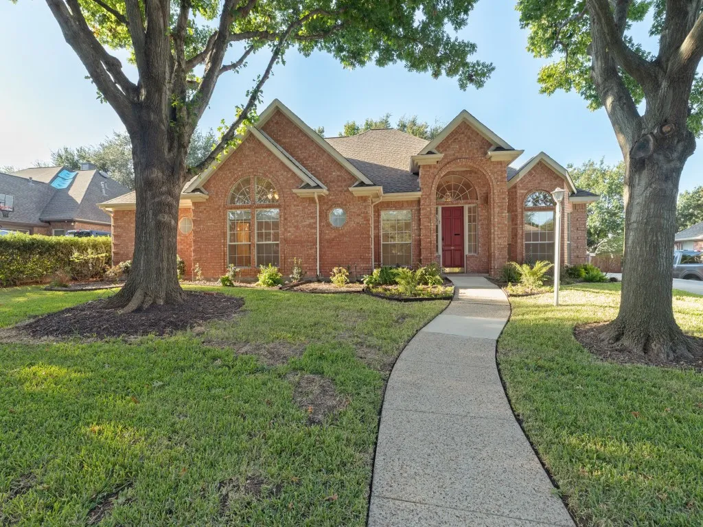 Brick exterior featuring multiple gables, an arched entryway, arched window detailing, and mature trees on the property