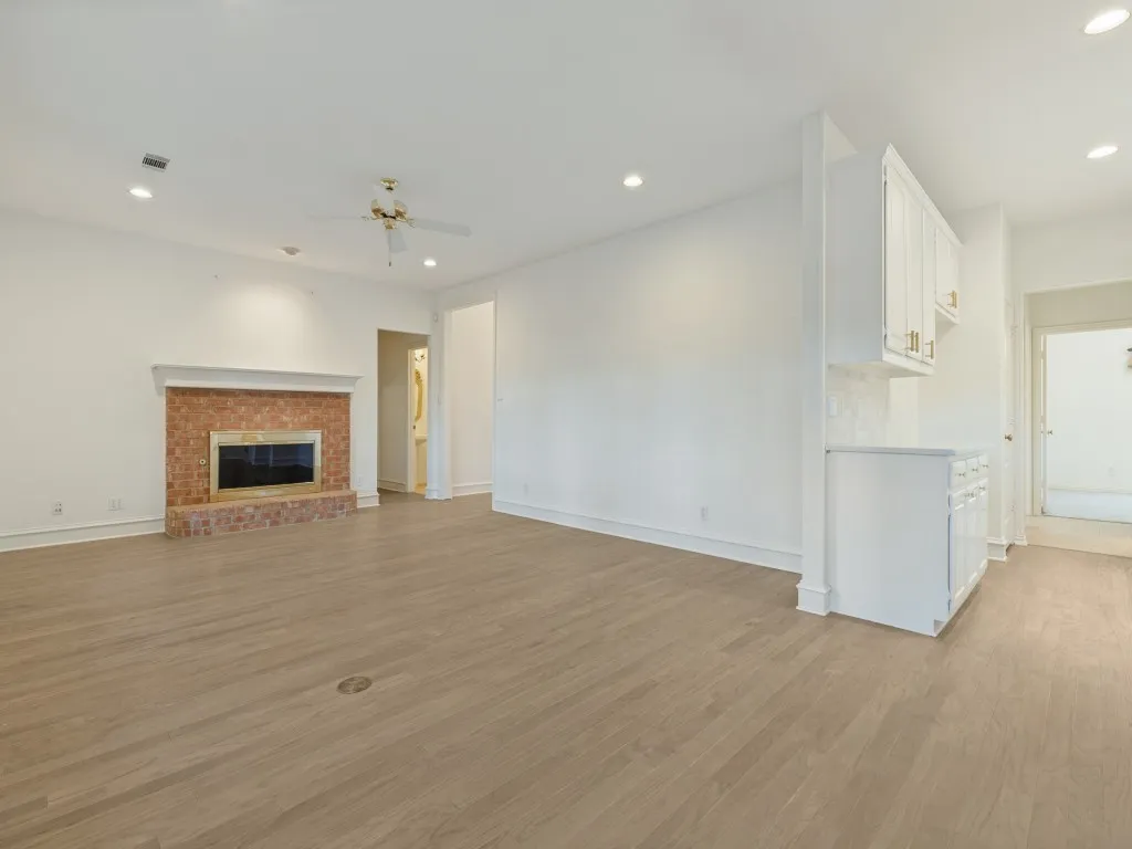Living area featuring wood-finish flooring, recessed lighting, a brick fireplace with a mantle, and built-in white cabinetry