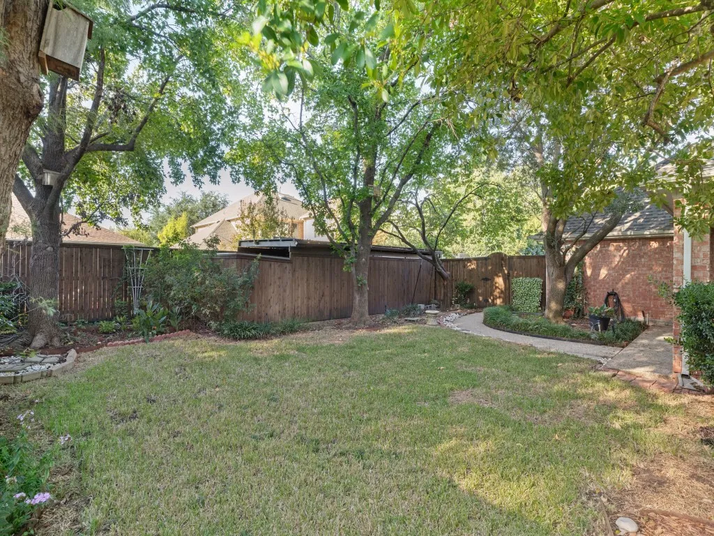 Backyard featuring a grass lawn, mature trees, wood privacy fencing, and a stone-paver walkway