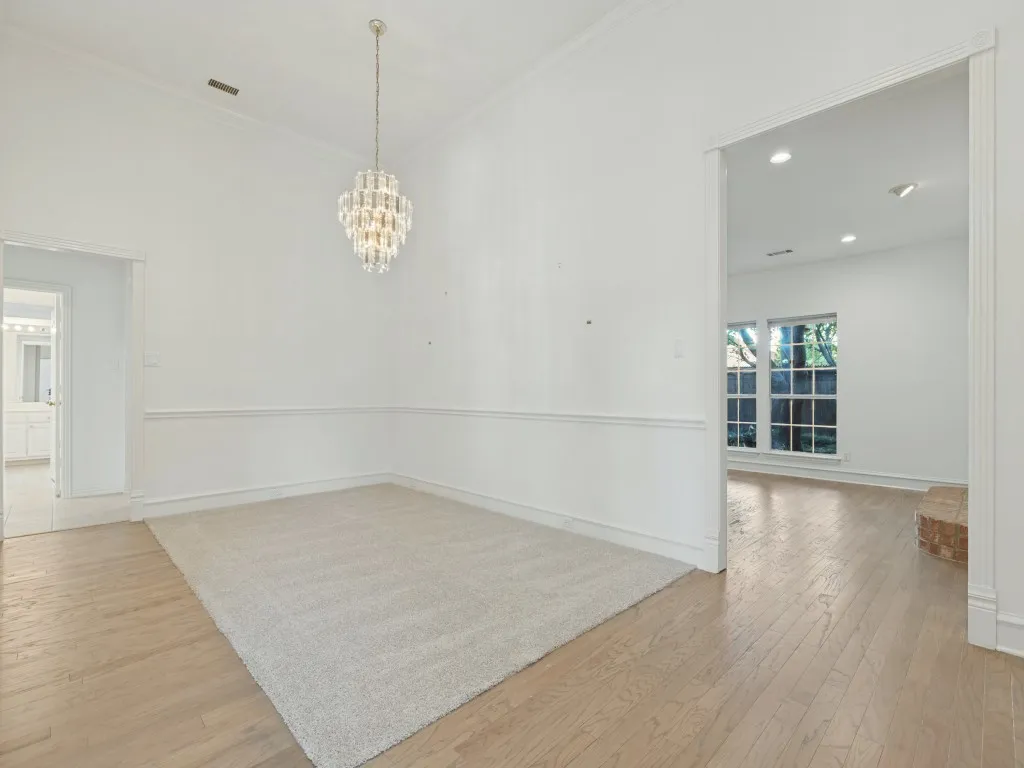 High ceilings featuring a tiered crystal chandelier, chair rail molding, and wood-finish flooring