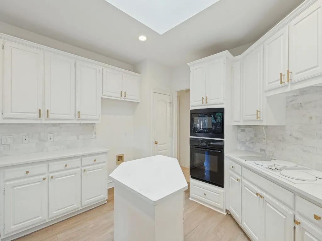 Kitchen featuring white shaker-style cabinetry, a central island with a solid surface countertop, stone-finish backsplash, recessed lighting, and built-in double wall ovens
