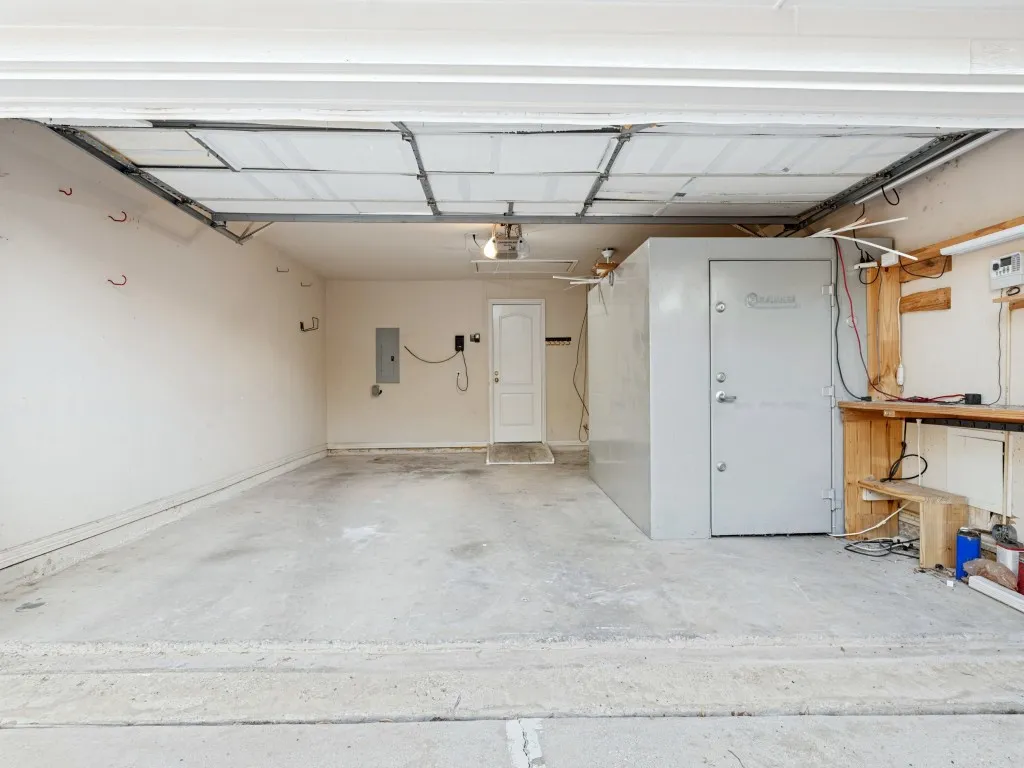 Multi-car garage featuring a concrete floor, overhead door, built-in metal storage vault, and integrated wooden workbench