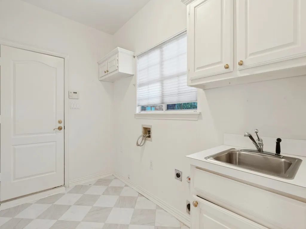 Utility area featuring white built-in cabinetry, a stainless steel drop-in sink with a metal faucet, geometric tile flooring, and a solid-core door