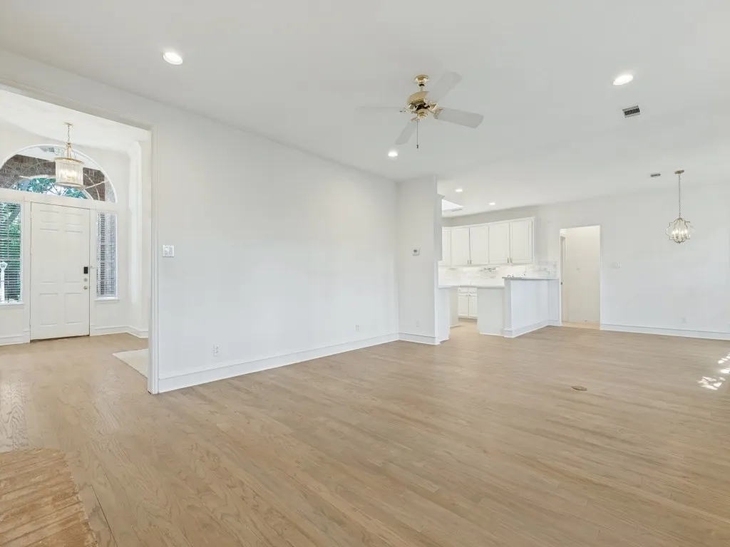 Open-concept interior featuring light wood-finish flooring, recessed lighting, a ceiling fan, white cabinetry, and a high-arched entryway