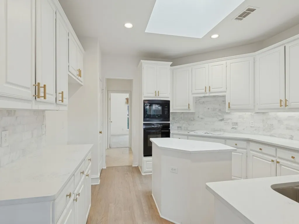 Kitchen featuring white shaker-style cabinetry with gold-tone hardware, stone-finish backsplash, quartz countertops, integrated double oven, and recessed ceiling lighting