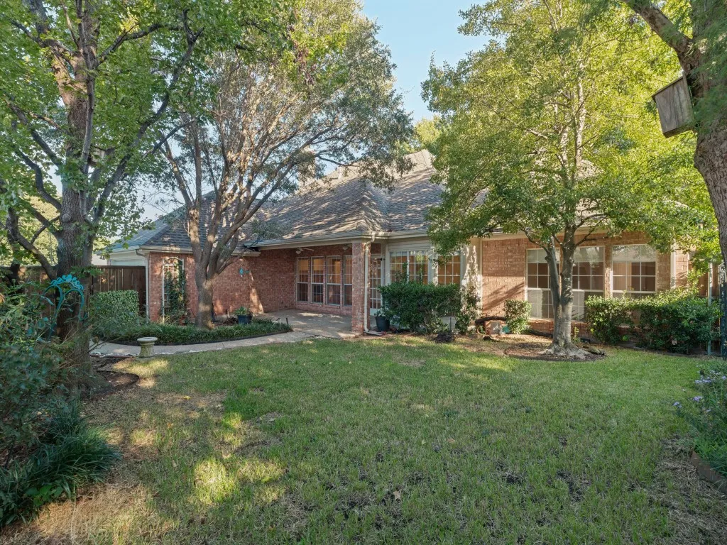 Backyard featuring a brick exterior, stone-paved patio, expansive grass lawn, mature trees, and privacy fencing
