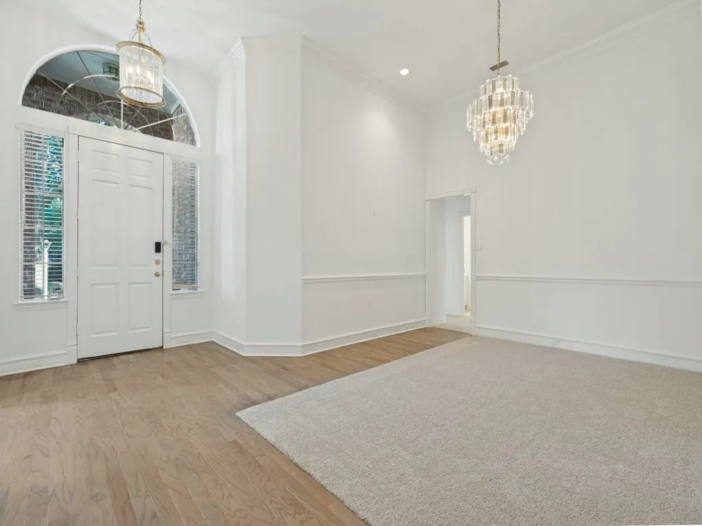 Entrance featuring an arched transom window, crystal-style chandeliers, decorative chair rail molding, wood-finish flooring, and wall-to-wall carpeting