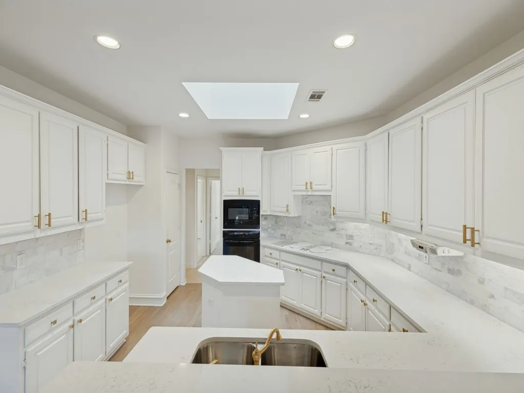 Kitchen featuring white shaker-style cabinetry, solid-surface countertops, a center island, recessed ceiling lighting, and a skylight