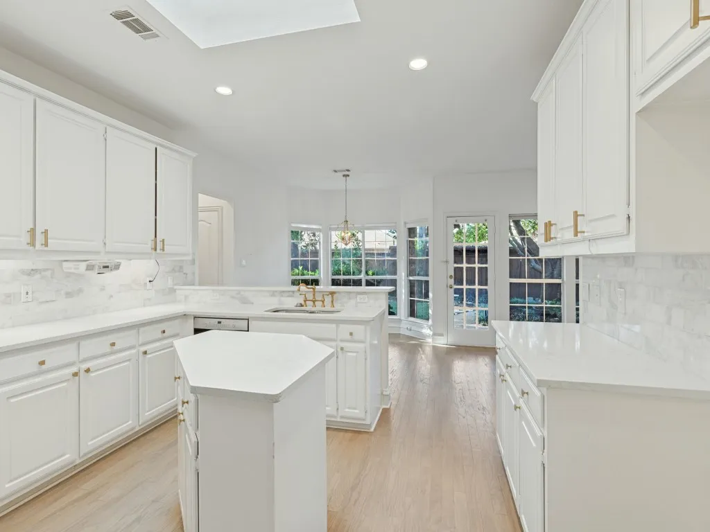 Kitchen featuring white cabinetry with gold-tone hardware, light-toned countertops, stone tile backsplash, wood-finish flooring, and a multi-sided center island