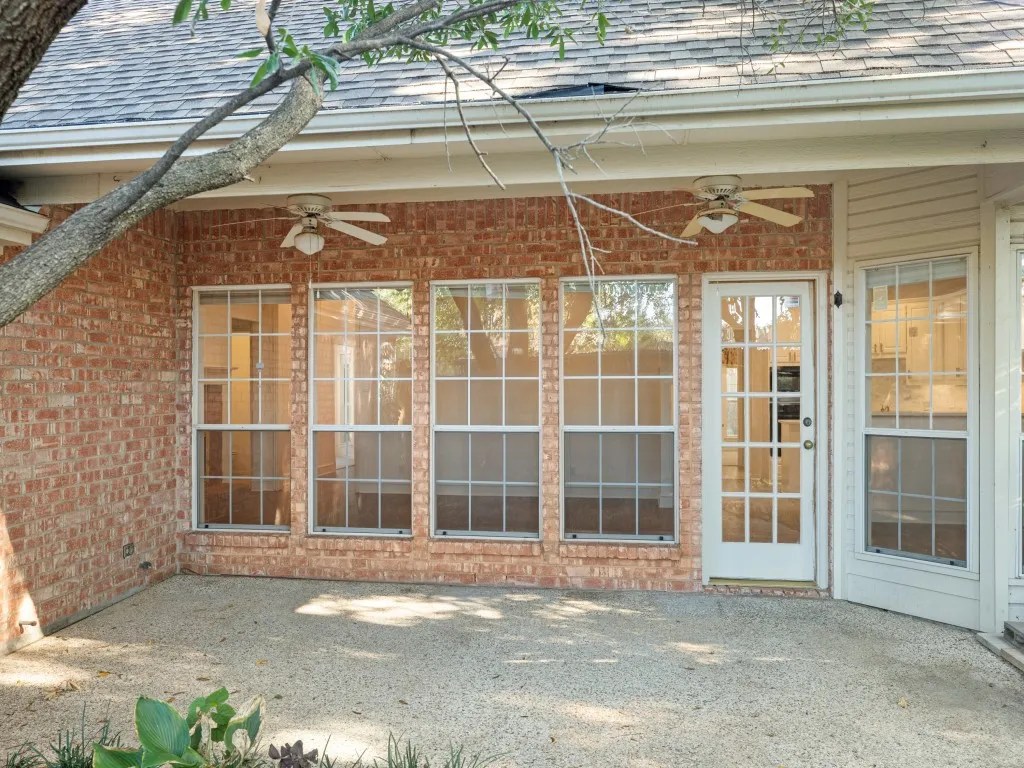 Covered brick patio featuring a concrete floor, dual ceiling fans, grid-pane windows, and a glass-paneled exterior door