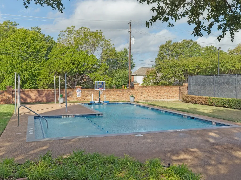 Swimming pool with aggregate surround, brick perimeter wall, and manicured landscaping