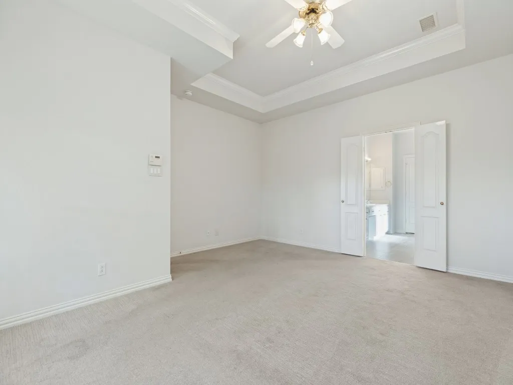 Room featuring a tray ceiling, neutral carpeting, and a ceiling-mounted light fixture with fan