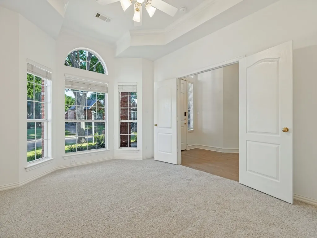 Room with tray ceilings, neutral carpeting, multi-pane bay windows with an arched transom, and double-panel doors