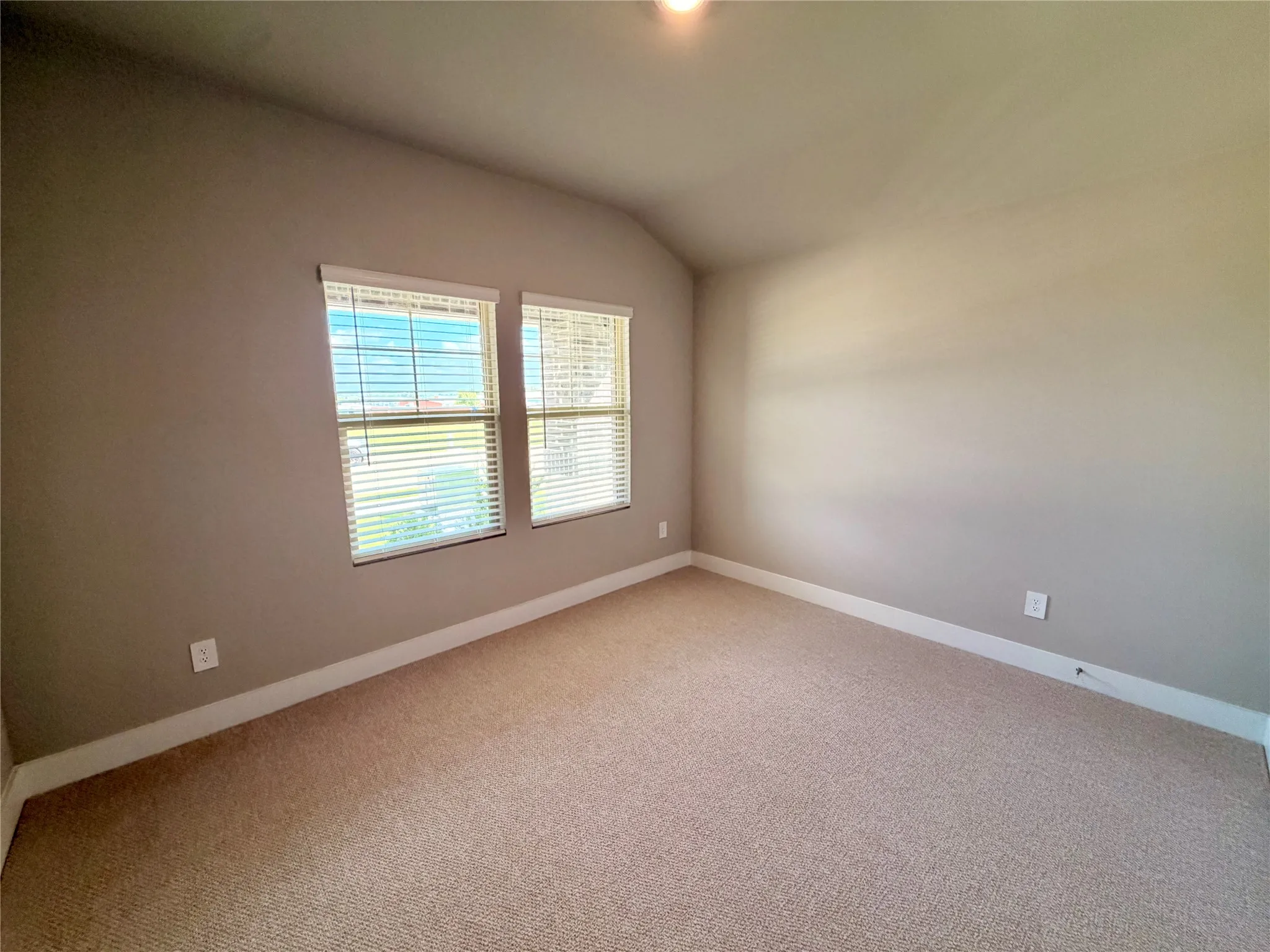 Neutral-toned room featuring a vaulted ceiling, wall-to-wall carpeting, and double windows with installed blinds