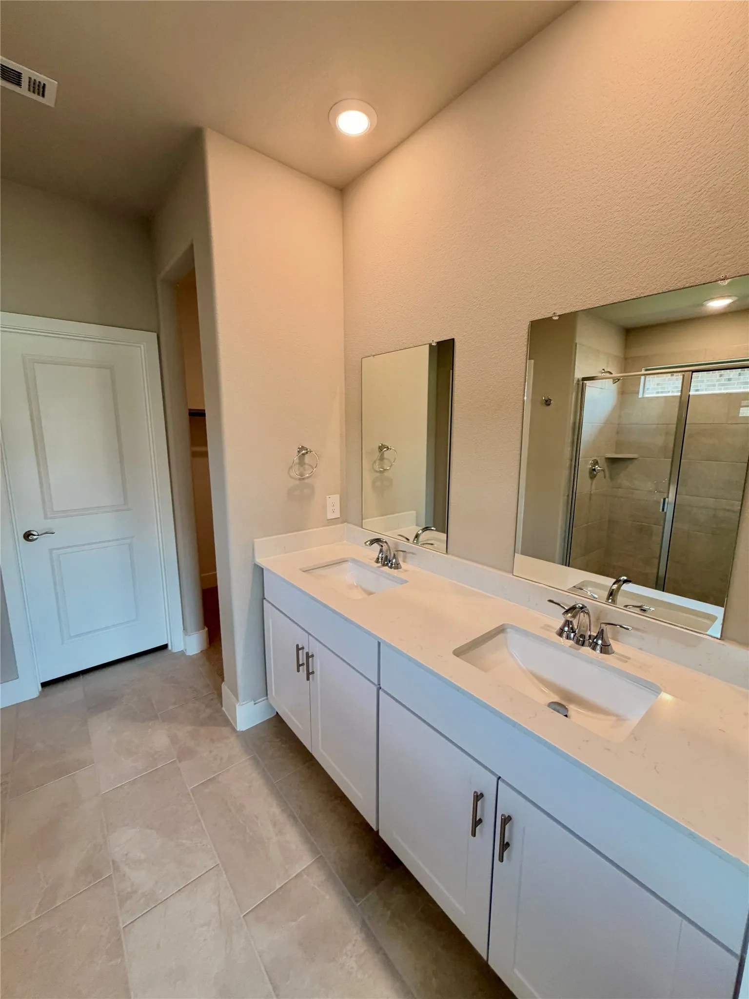 Double vanity featuring white cabinetry, light-toned stone-finish countertops, dual under-mount sinks, and large frameless mirrors