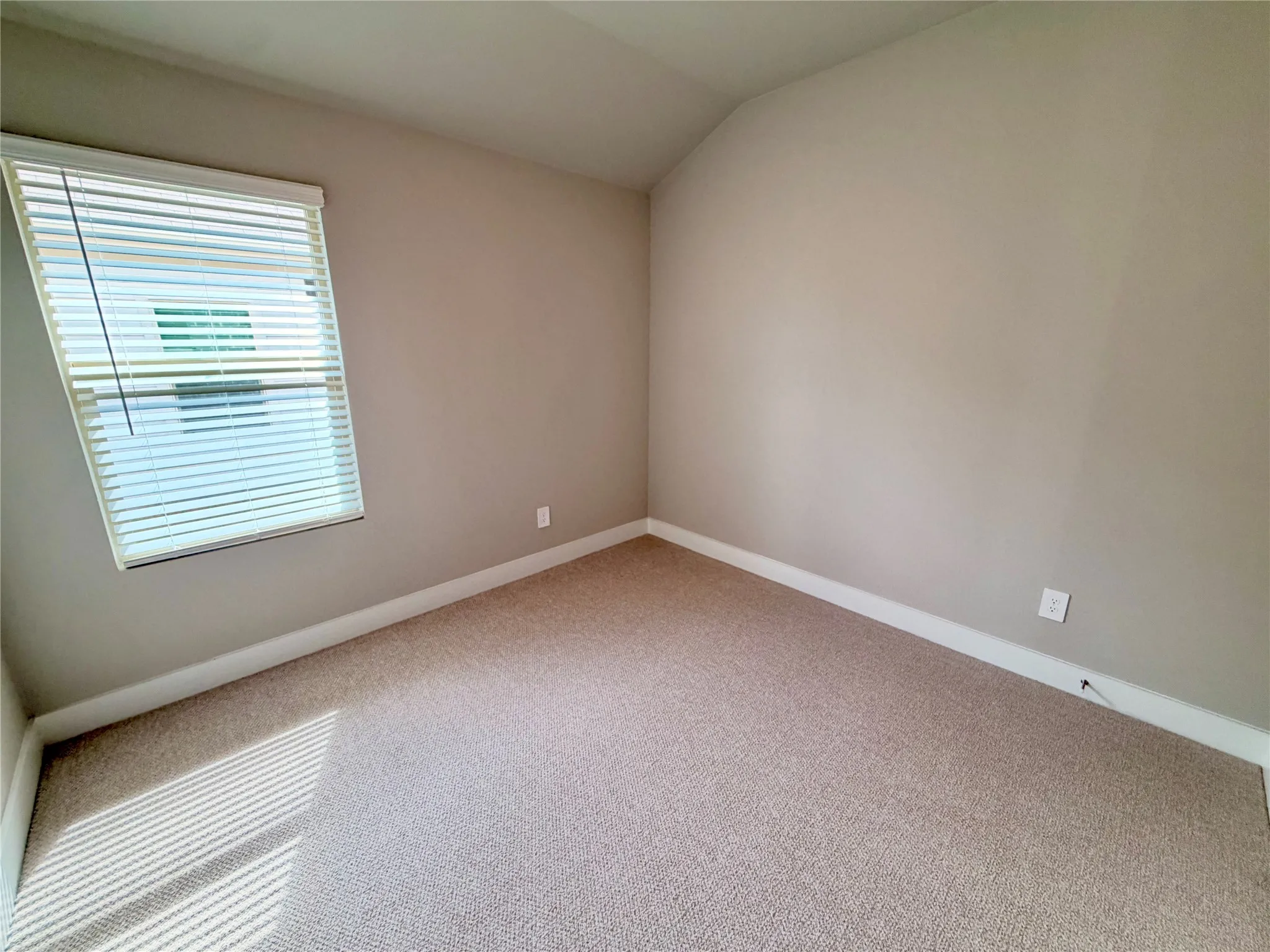 Room featuring neutral-toned carpeting, vaulted ceilings, and a window with horizontal blinds