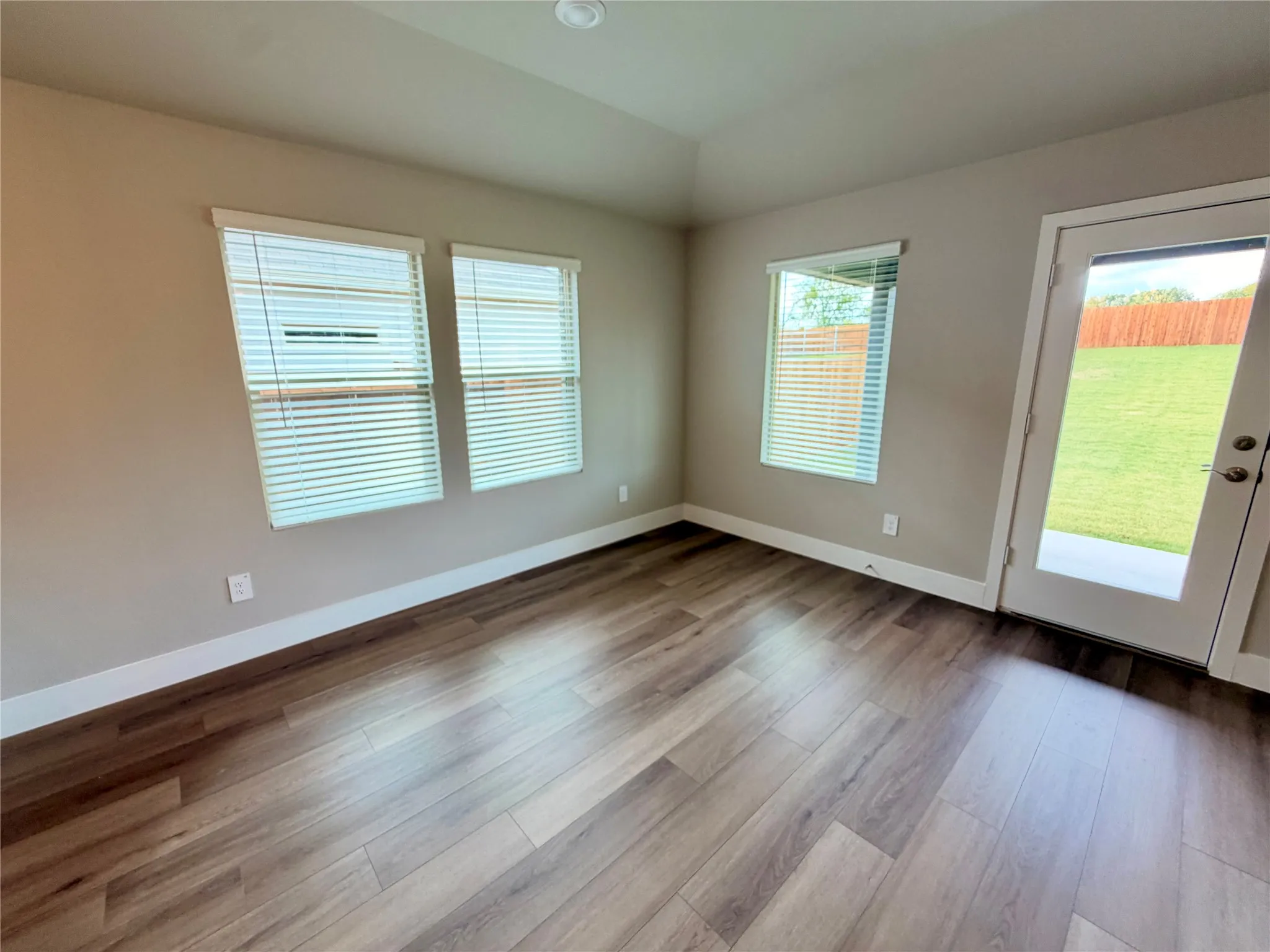 Neutral-toned interior featuring wood-finish flooring, tray ceiling, multiple windows, and a glass-paneled exterior door