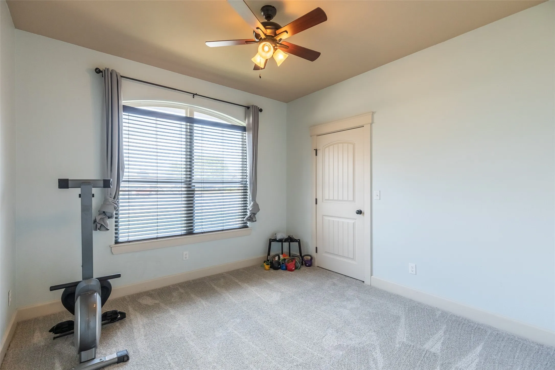 Neutral-toned wall-to-wall carpeting, arch-top window with integrated blinds, and multi-light ceiling fan