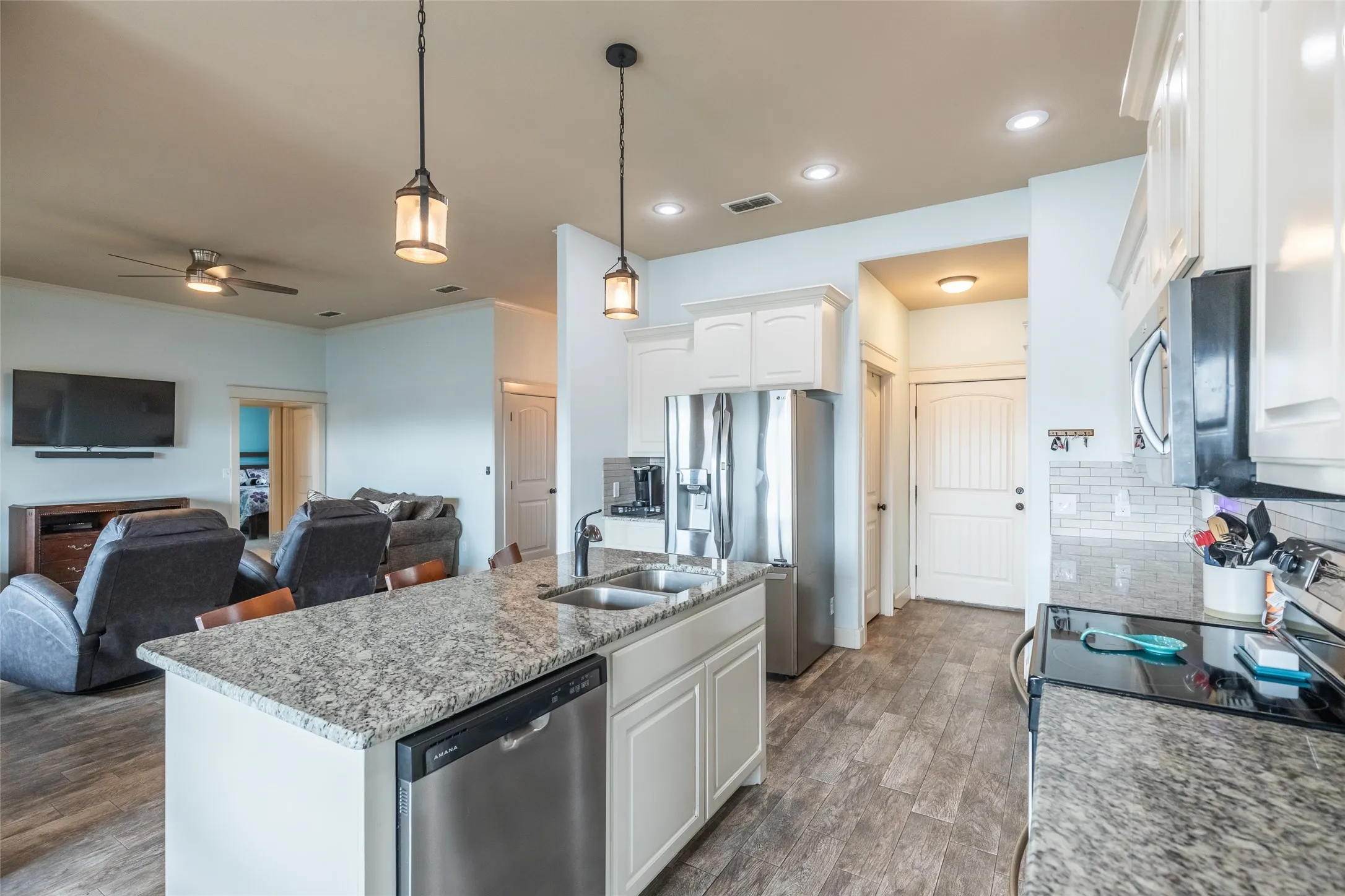 Kitchen featuring a central island with a stone countertop and double-basin sink, white shaker-style cabinetry, stainless steel appliances, pendant lighting, and wood-finish flooring