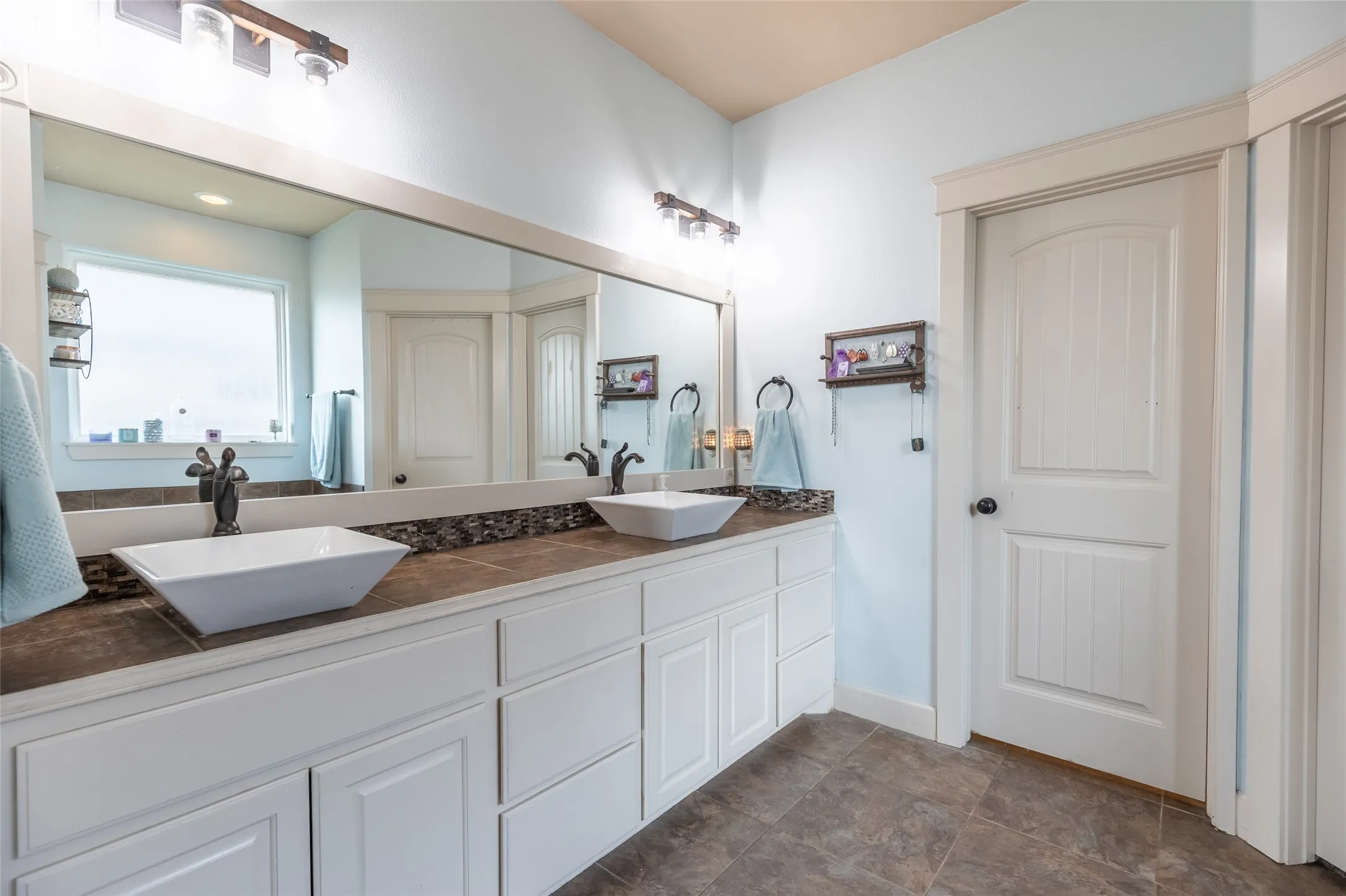 Dual vanity featuring white shaker-style cabinetry, rectangular vessel sinks, stone-finish countertops, and dual wall-mounted light fixtures