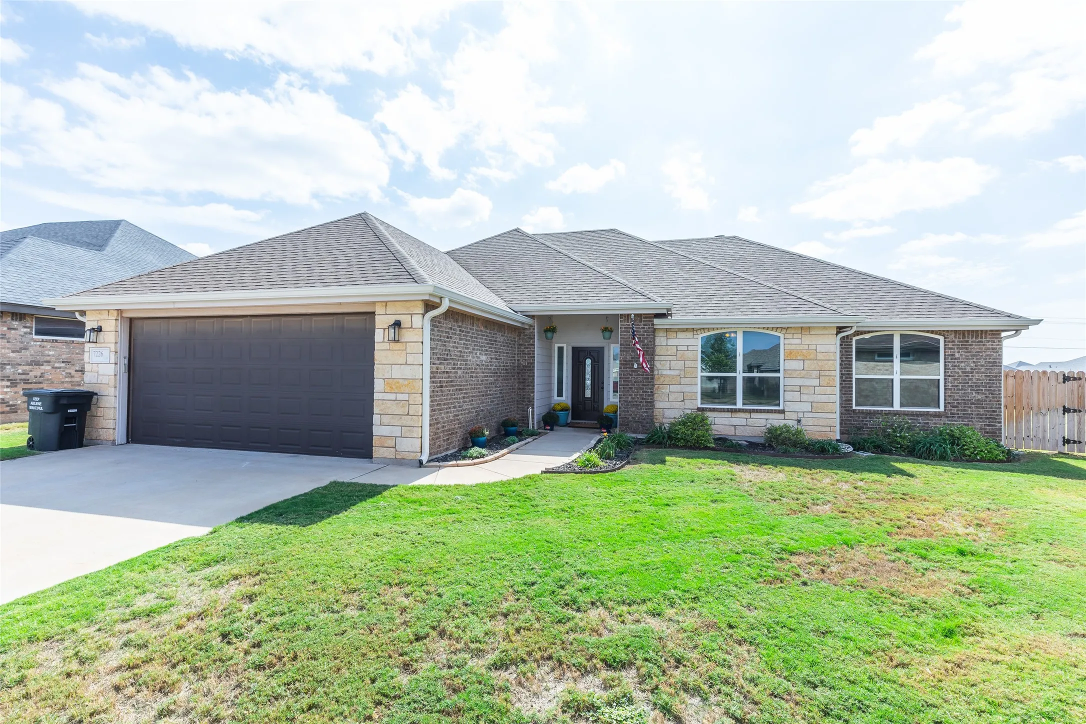 Exterior facade featuring a combination of brick and stone masonry, hip roof construction, two-car garage, arched window accents, and a concrete driveway