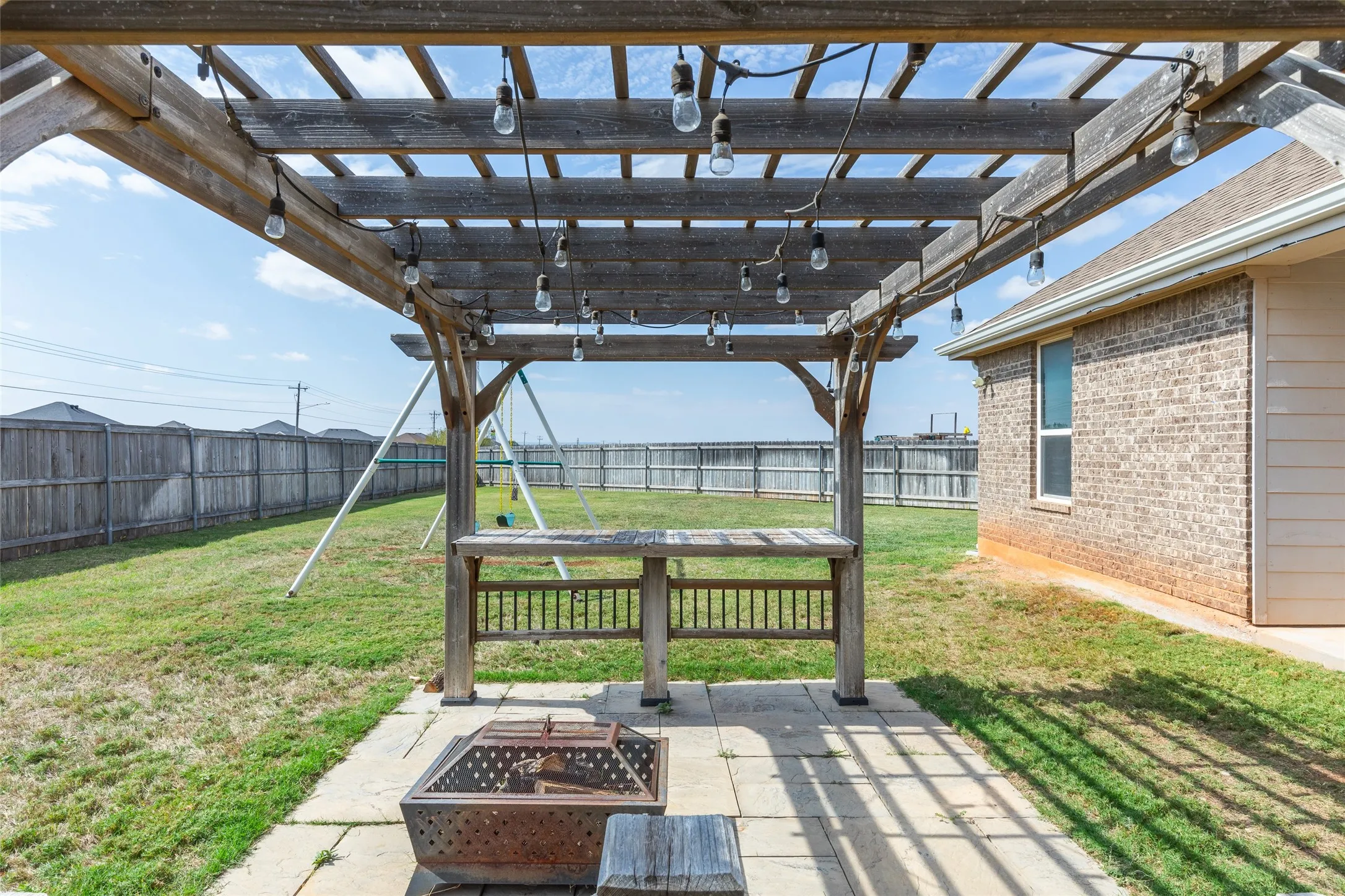Backyard featuring a wooden pergola with integrated string lighting, a built-in counter, and a concrete paver patio