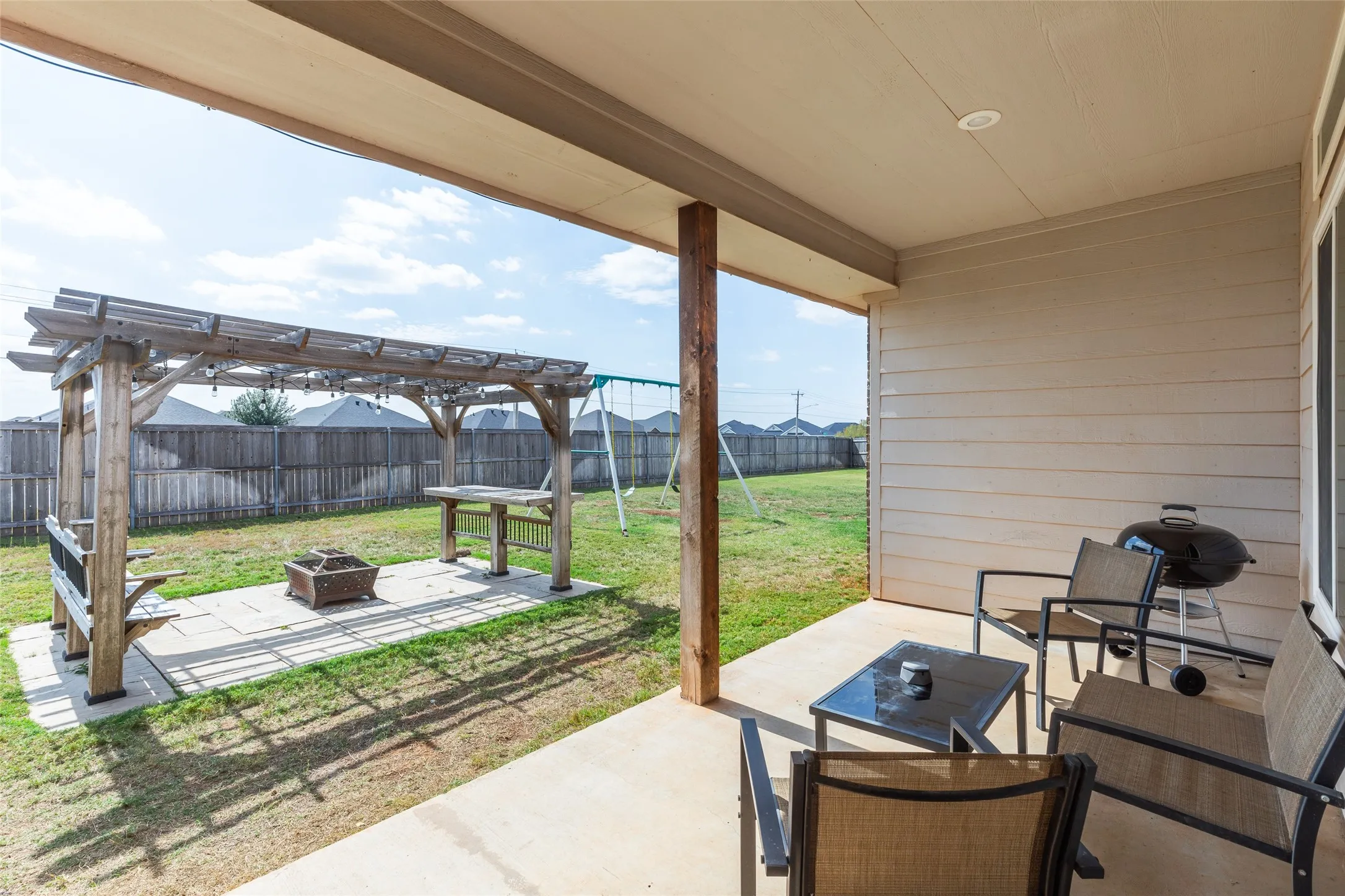 Covered concrete patio with horizontal siding, featuring a wooden pergola and paved outdoor area