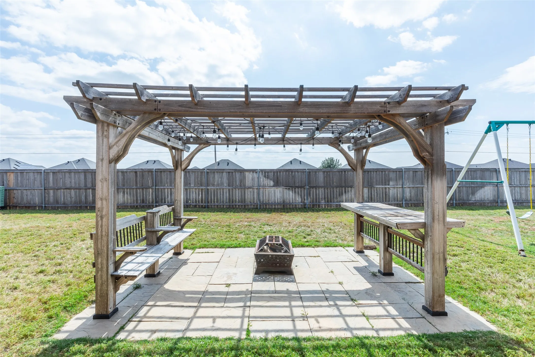 Backyard area featuring a wooden pergola with integrated string lighting, a concrete paver patio, and built-in wooden benches