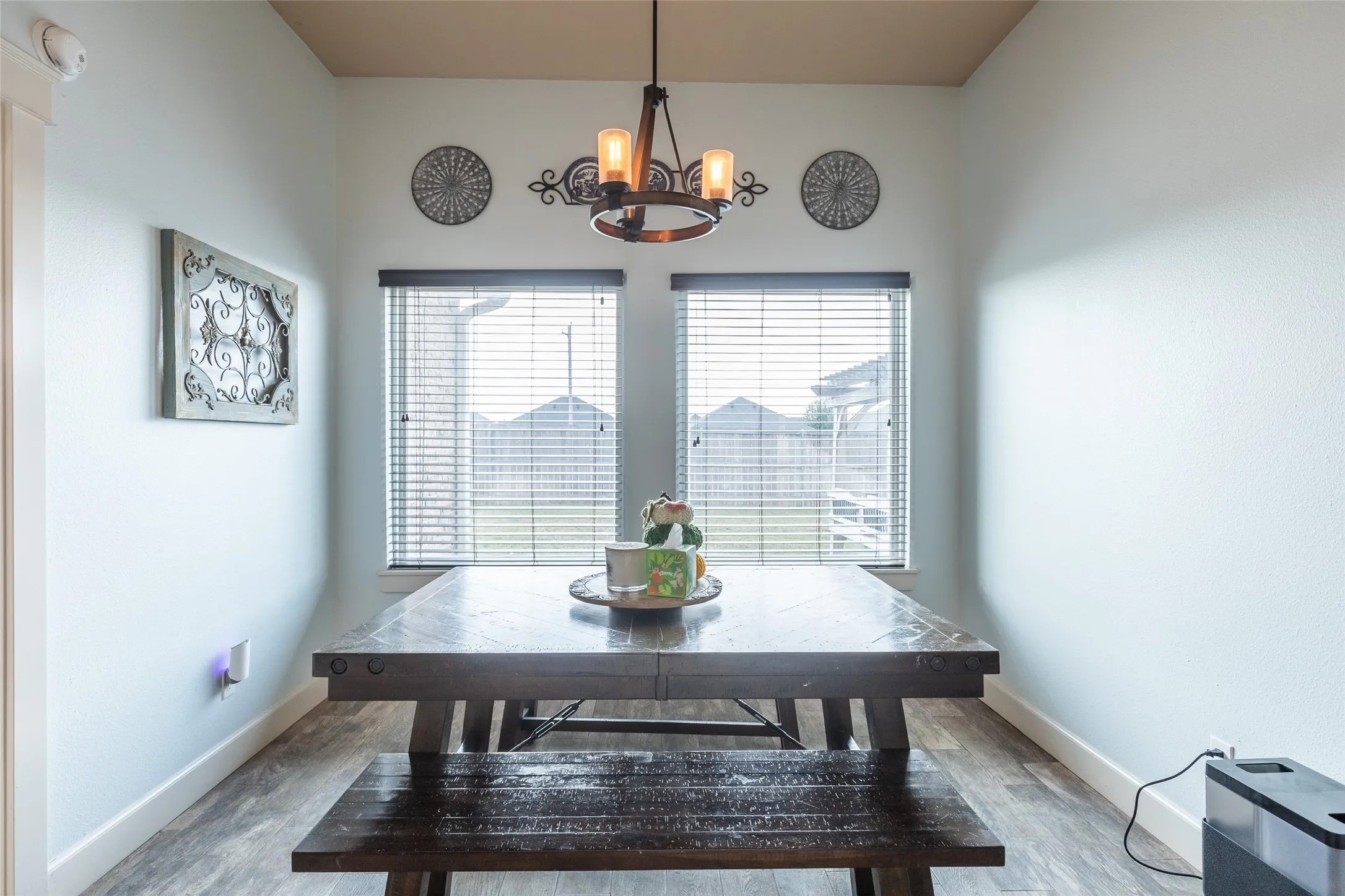 High-ceilinged room featuring wood-finish flooring, twin windows with horizontal blinds, and a suspended iron-style multi-light fixture