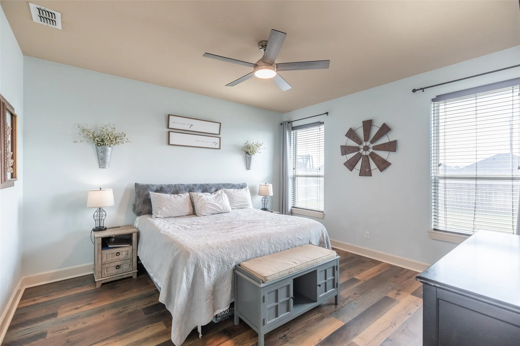 Room featuring wood-finish flooring, a multi-blade ceiling fan with integrated lighting, and dual windows equipped with horizontal blinds