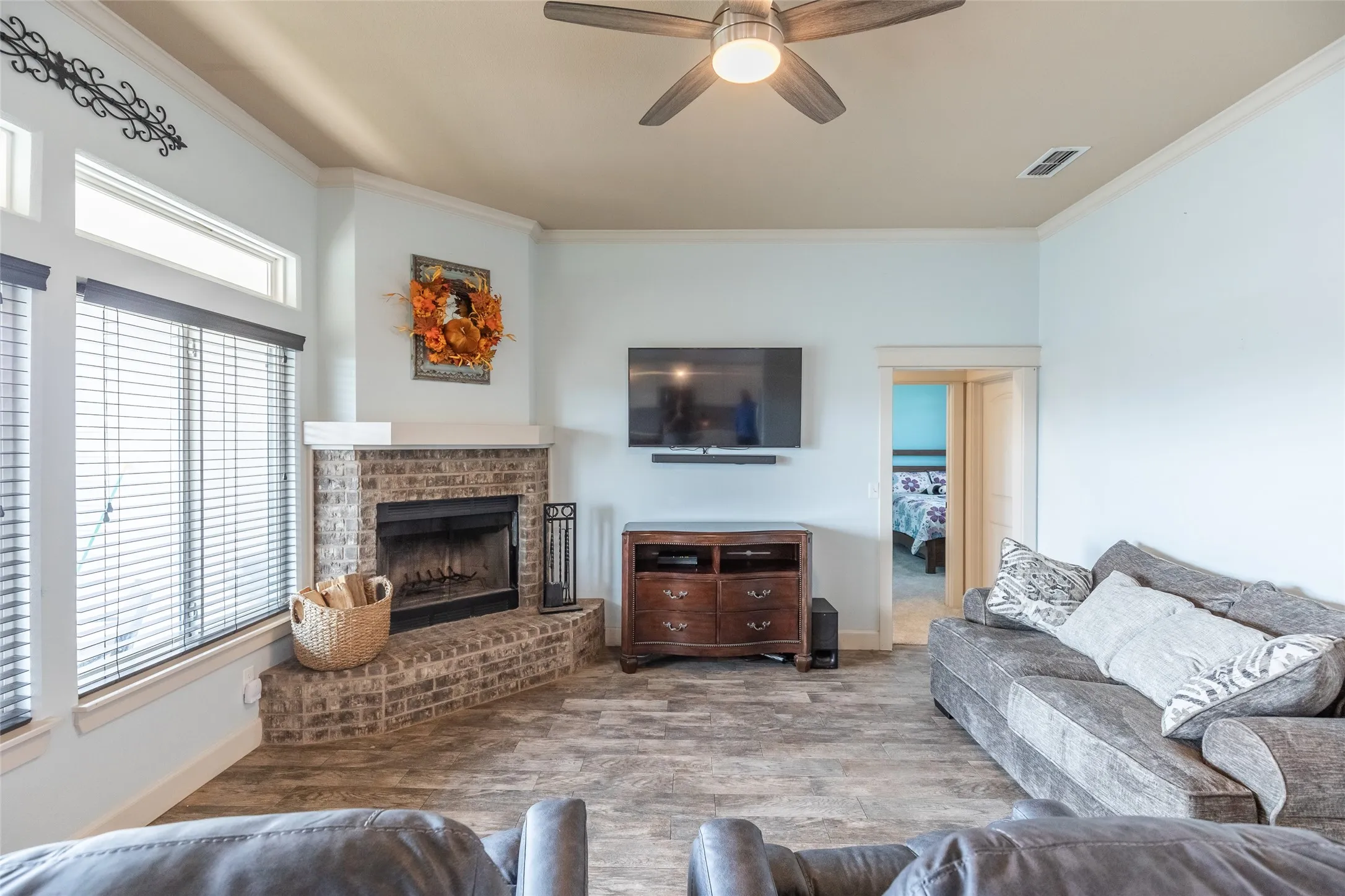 Corner fireplace featuring brick masonry construction, multi-pane windows with horizontal blinds, ceiling fan, and tile flooring