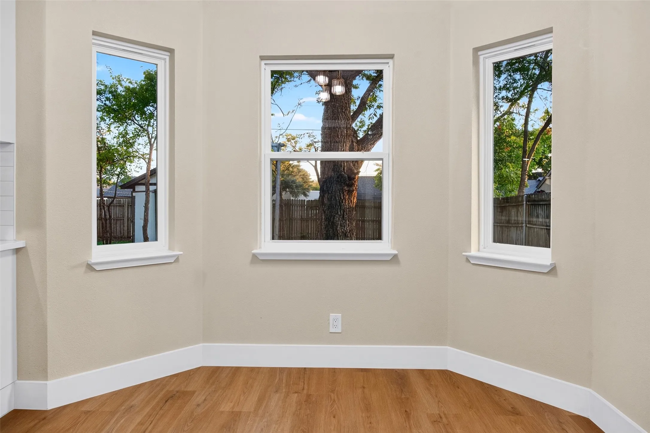 Bay area featuring three expansive windows with white trim and wood-finish flooring
