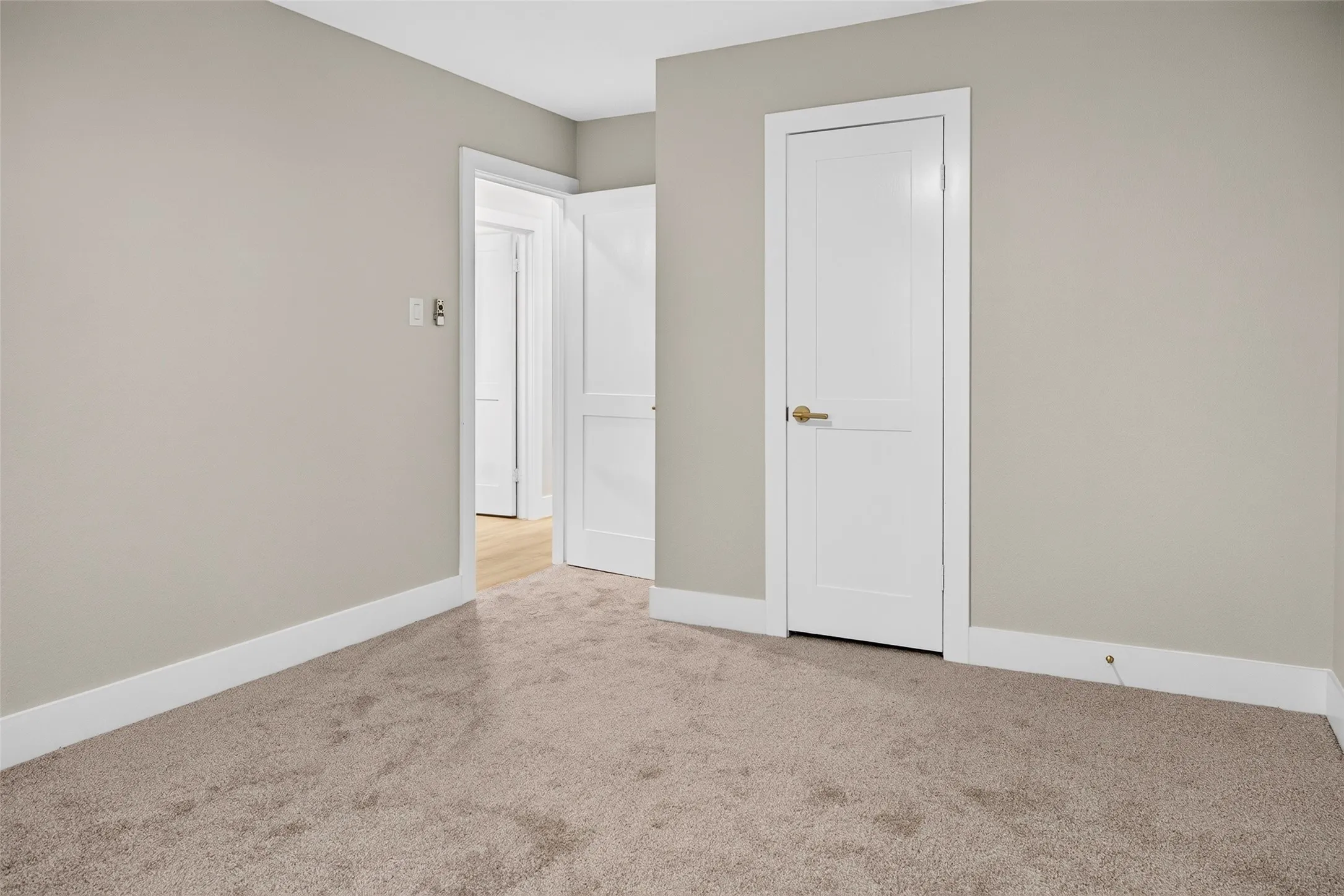 Neutral-toned interior space featuring wall-to-wall carpeting, white two-panel interior doors, and crisp white door casings