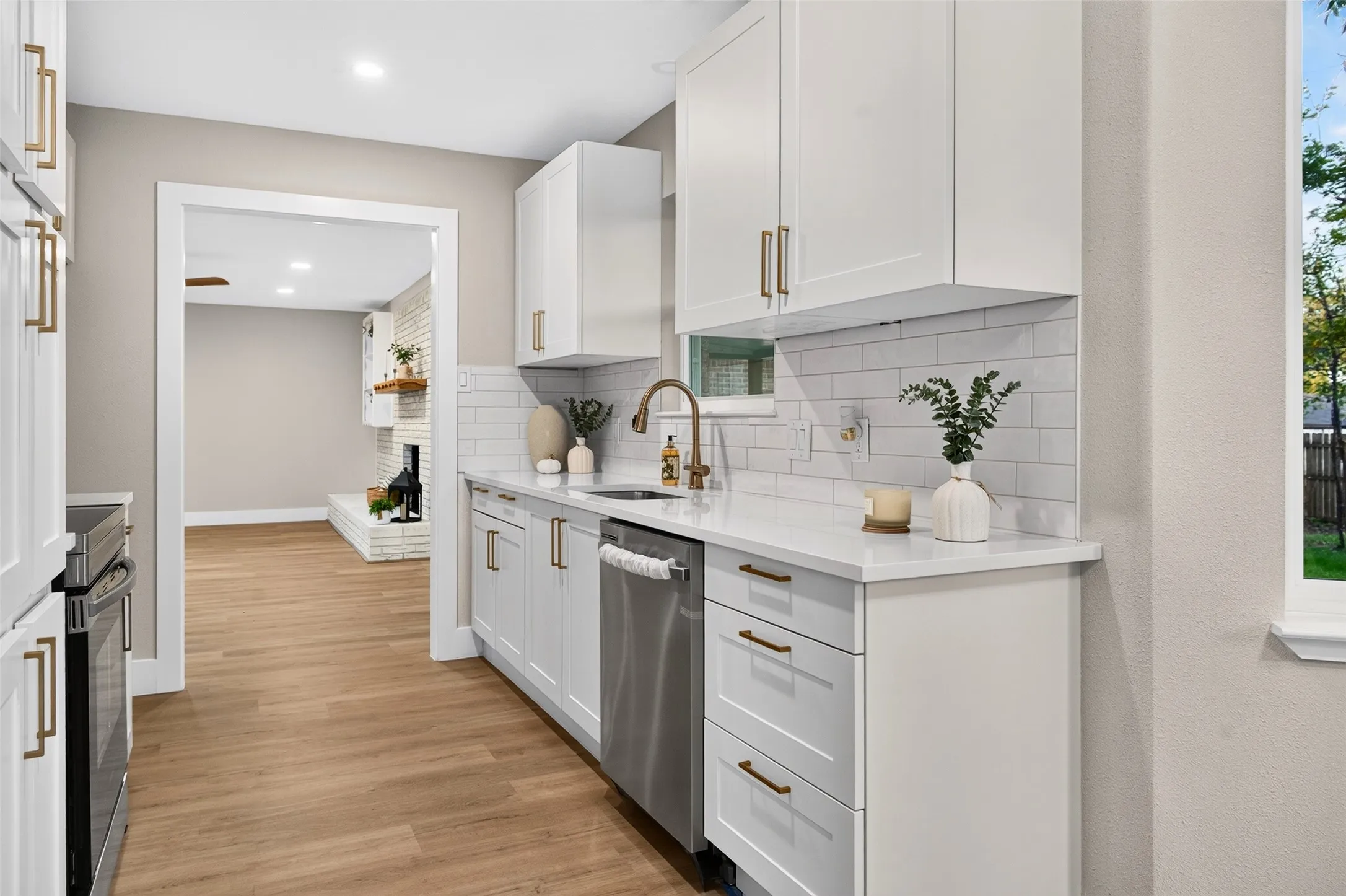 Kitchen featuring white shaker-style cabinetry, solid-surface countertops, a white subway tile backsplash, stainless steel dishwasher, and metallic hardware