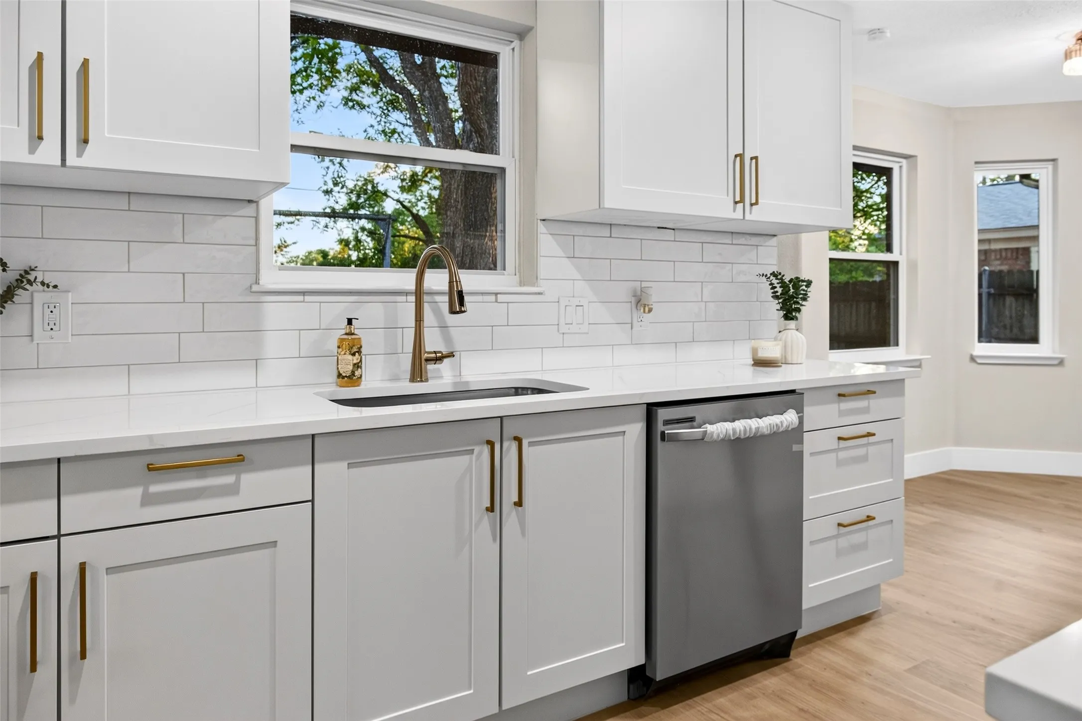 Kitchen featuring white Shaker-style cabinetry, quartz countertops, subway tile backsplash, stainless steel dishwasher, and gold-finish hardware