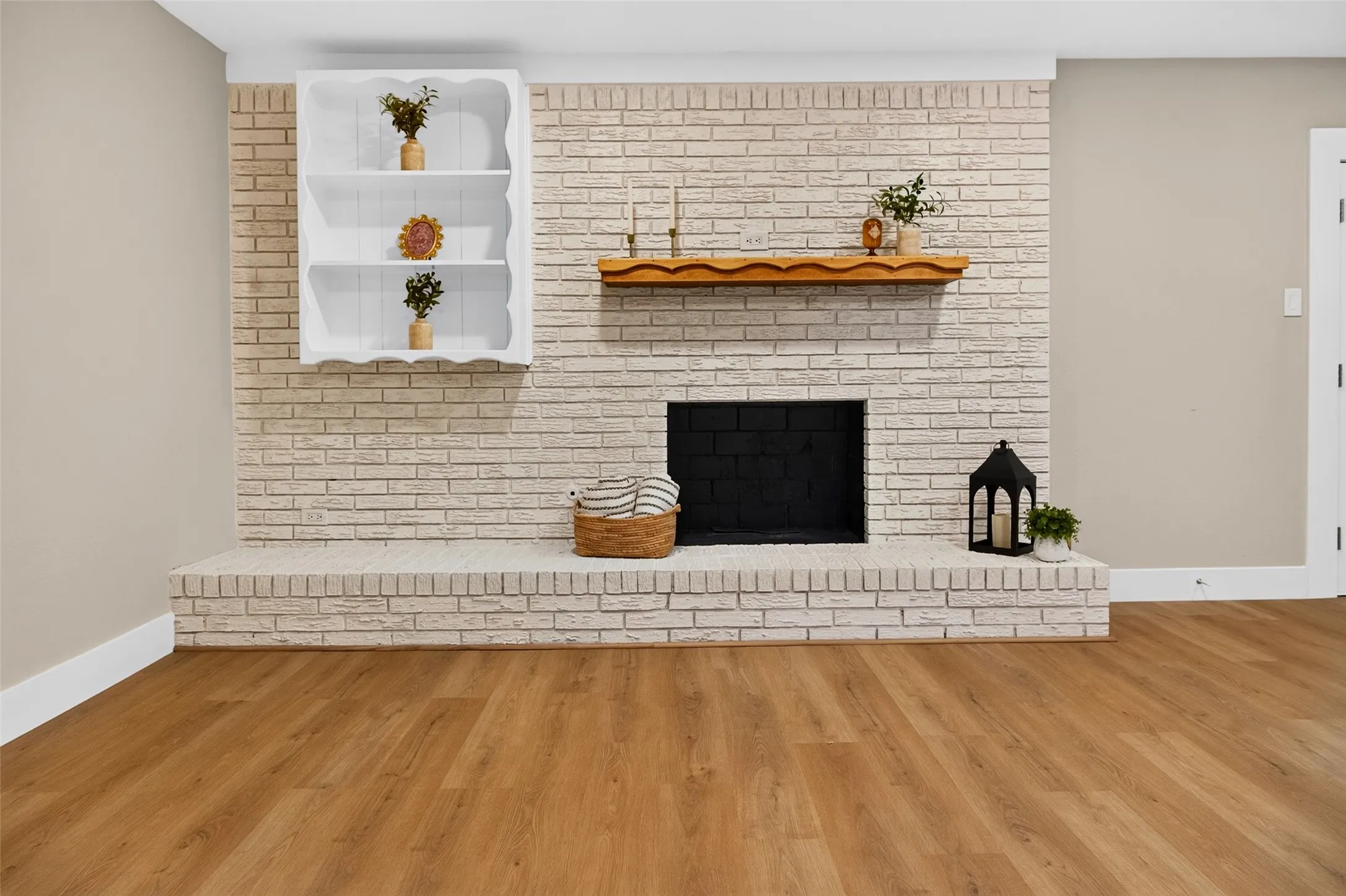 Floor-to-ceiling whitewashed brick fireplace featuring a wood mantel, raised masonry hearth, built-in recessed shelving, and wood-finish flooring