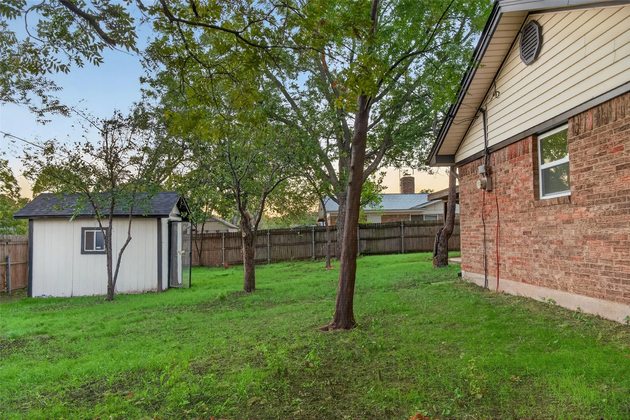 Exterior features include a brick and siding facade, a detached storage structure, mature trees, and wooden perimeter fencing