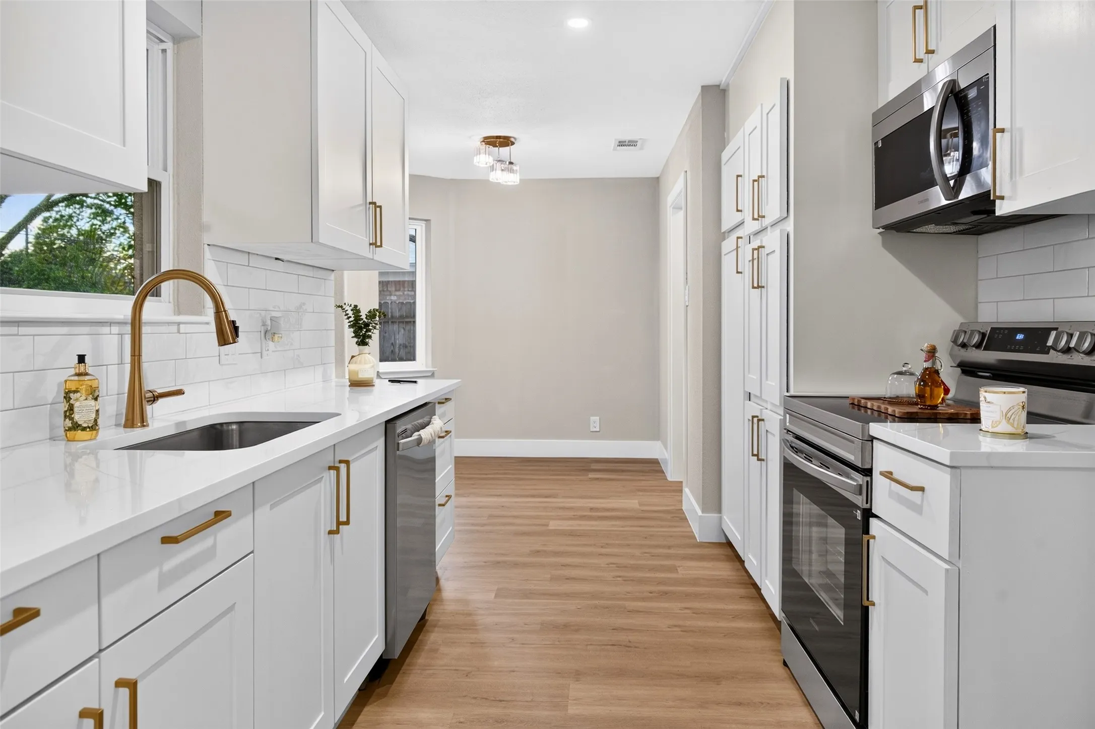 Kitchen featuring white Shaker-style cabinetry, quartz countertops, white subway tile backsplash, brass-finish hardware, and stainless steel appliances