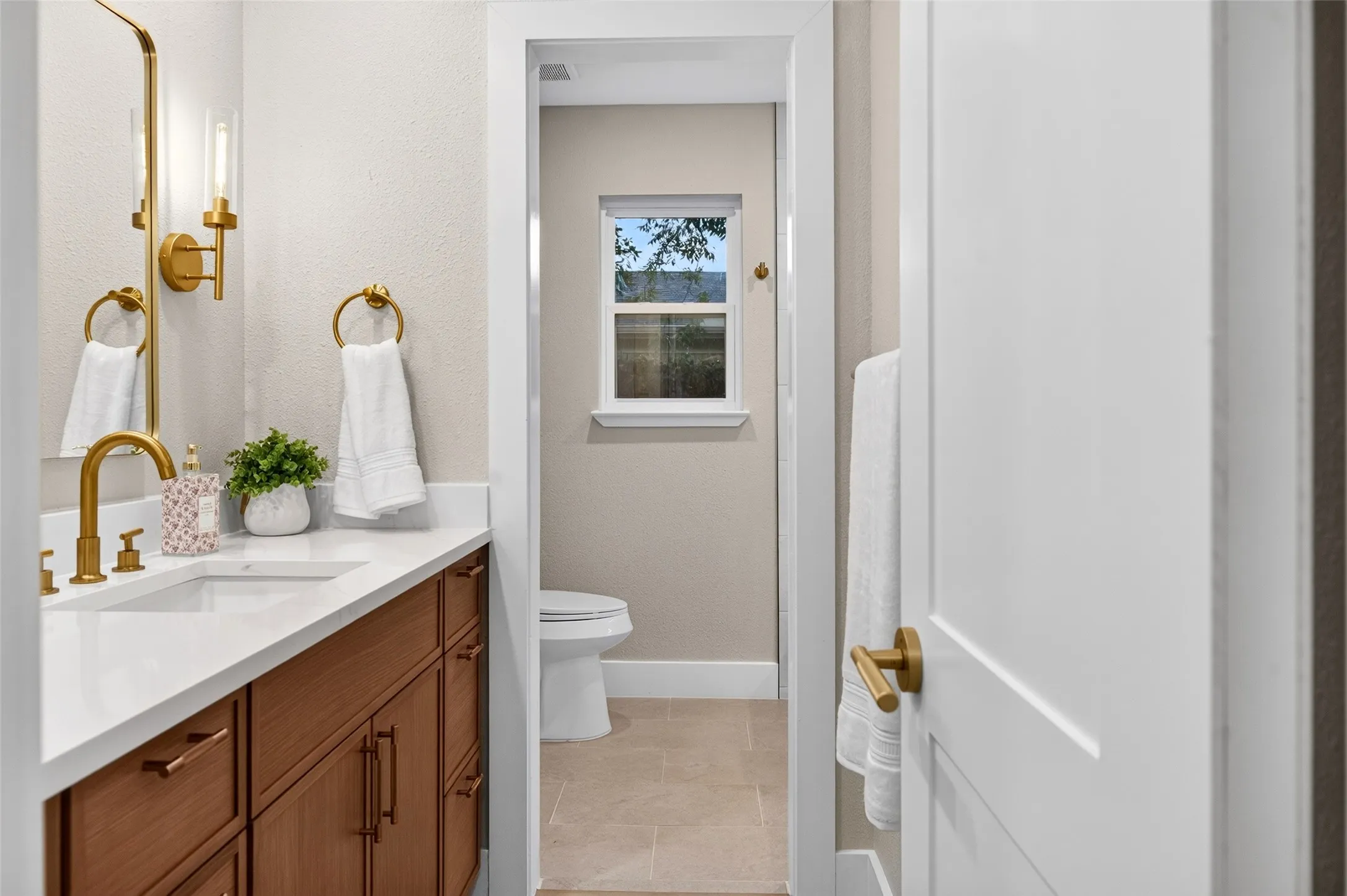 Bathroom featuring wood-finish cabinetry, white countertop with integrated sink, brass-tone hardware, wall-mounted light fixtures, and tile flooring