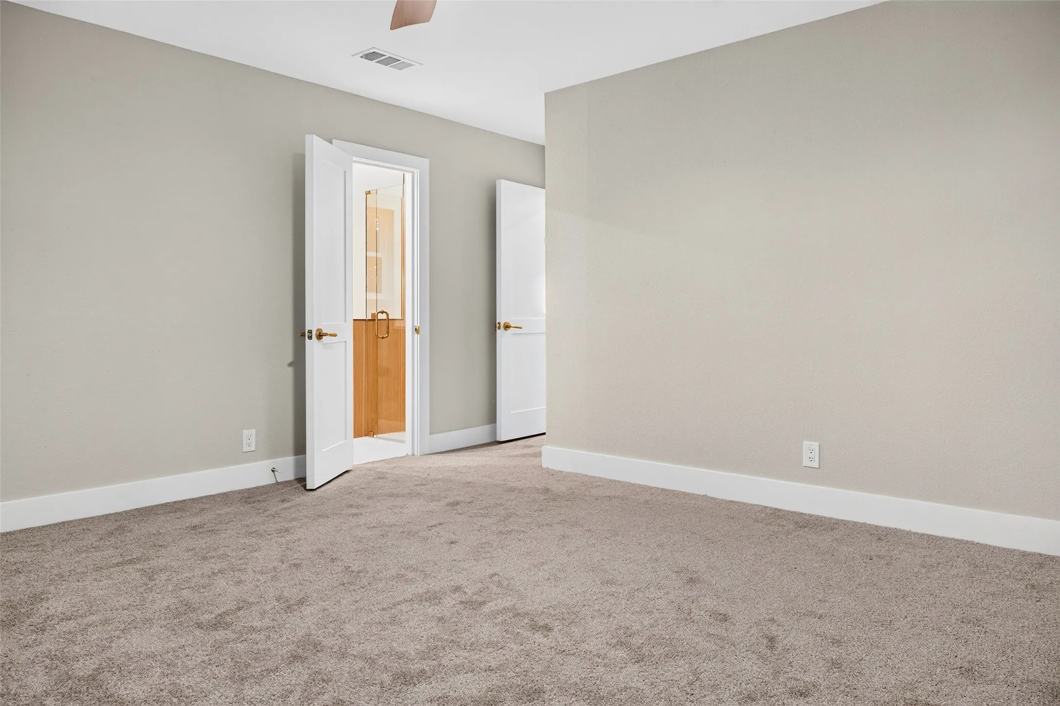 Neutral-toned interior space featuring plush wall-to-wall carpeting, crisp white interior doors with metallic hardware, and a ceiling-mounted fan