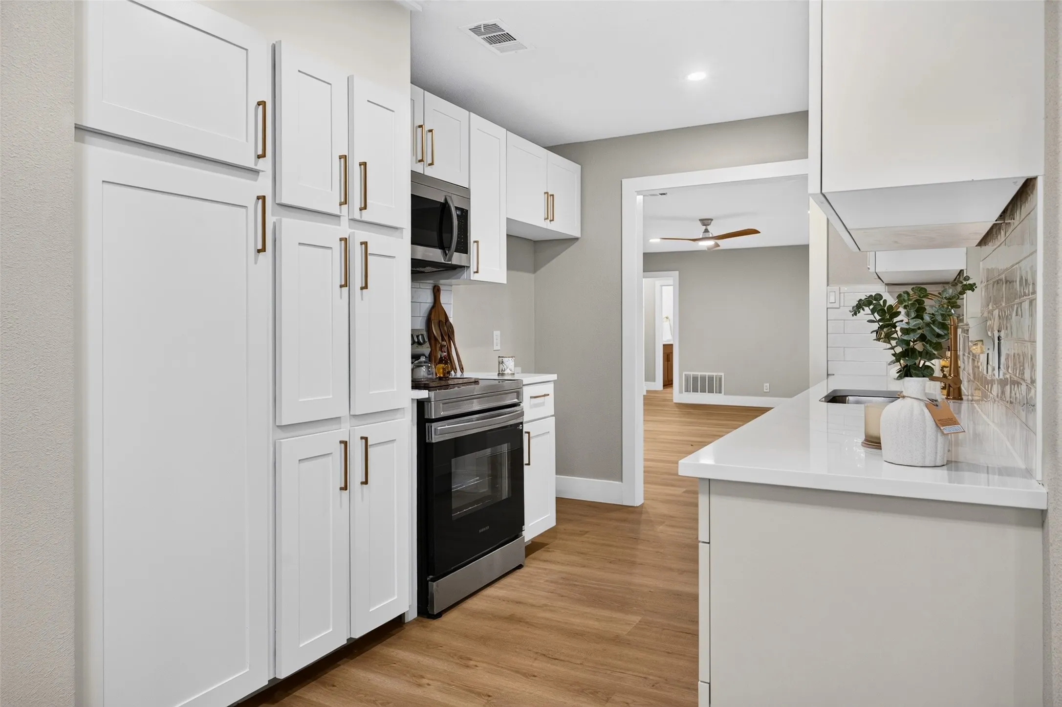 Kitchen featuring white shaker-style cabinetry, matte bronze hardware, quartz countertops, subway tile backsplash, and stainless steel appliances