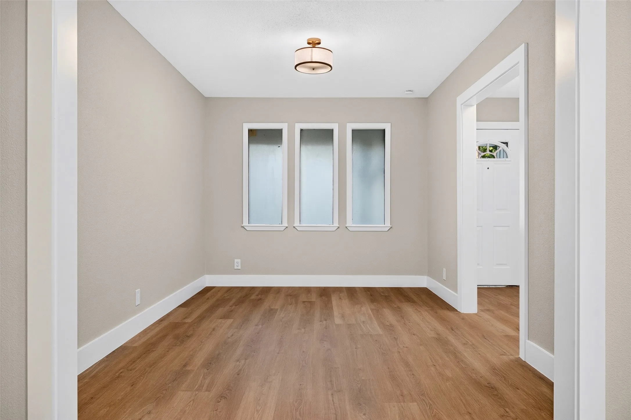 Room featuring wood-finish flooring, three vertical windows with white trim, and a modern drum-style ceiling light fixture