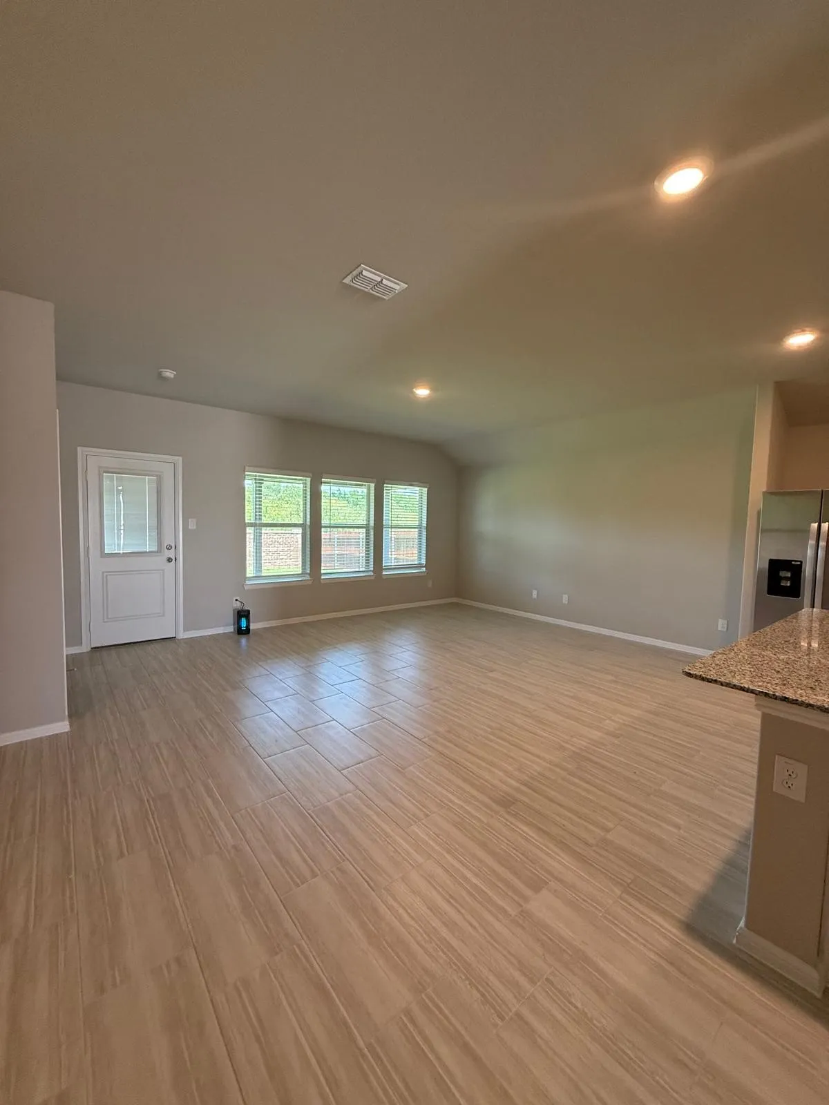 Open-concept area featuring wood-finish tile flooring, recessed lighting, neutral wall paint, and a trio of windows providing natural light