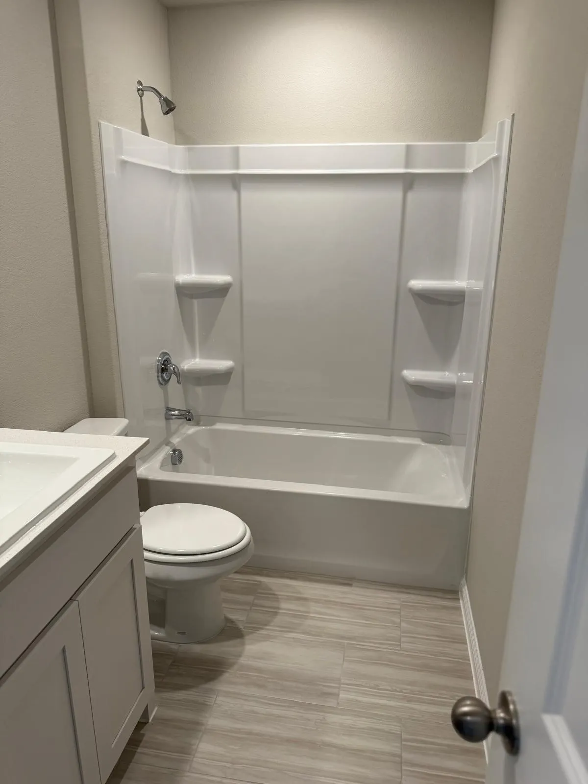 Bathroom featuring a white vanity cabinet with a integrated sink, wood-finish tile flooring, a porcelain toilet, and a white acrylic tub-shower combination with integrated shelving and chrome fixtures