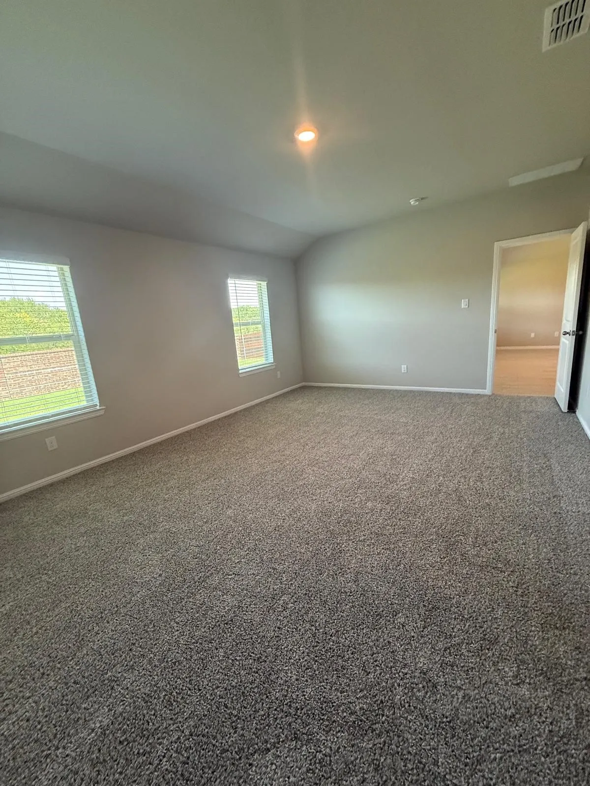 Neutral interior space featuring vaulted ceilings, neutral wall tones, plush wall-to-wall carpeting, and double-pane windows with horizontal blinds