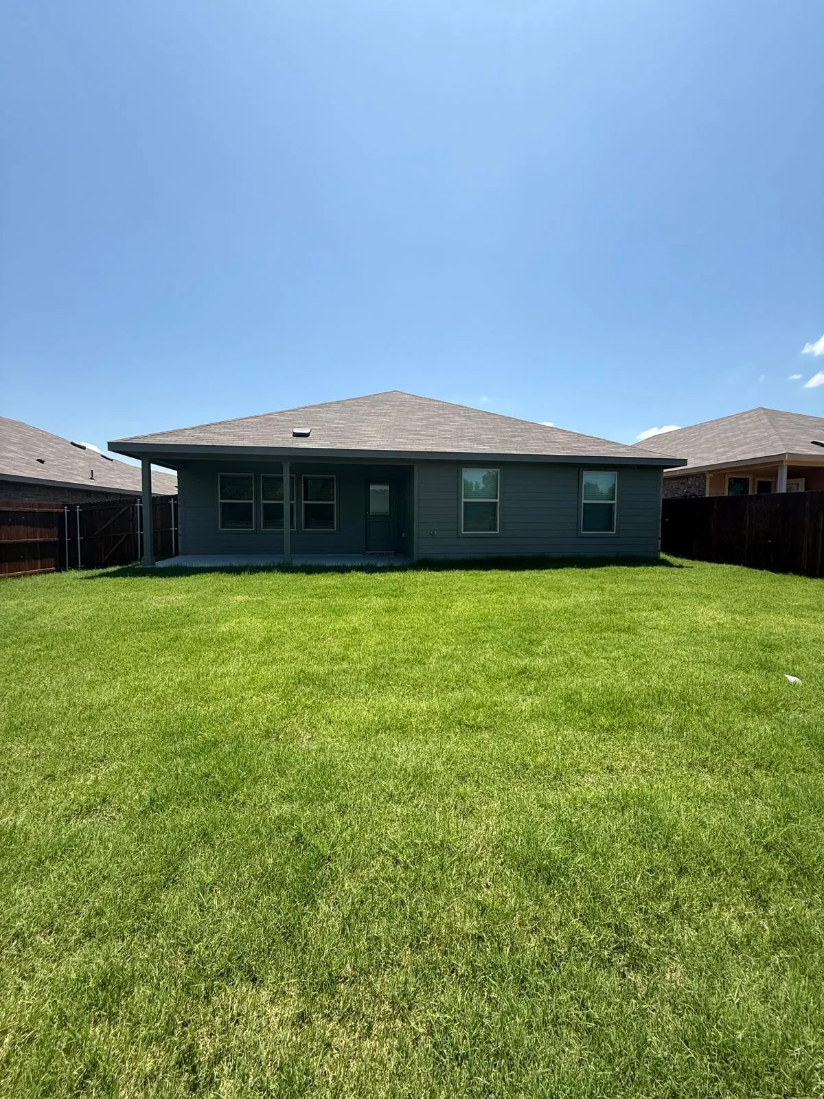 Exterior rear elevation featuring horizontal siding, a hipped roofline, an integrated covered patio, and enclosed yard space with wood fencing