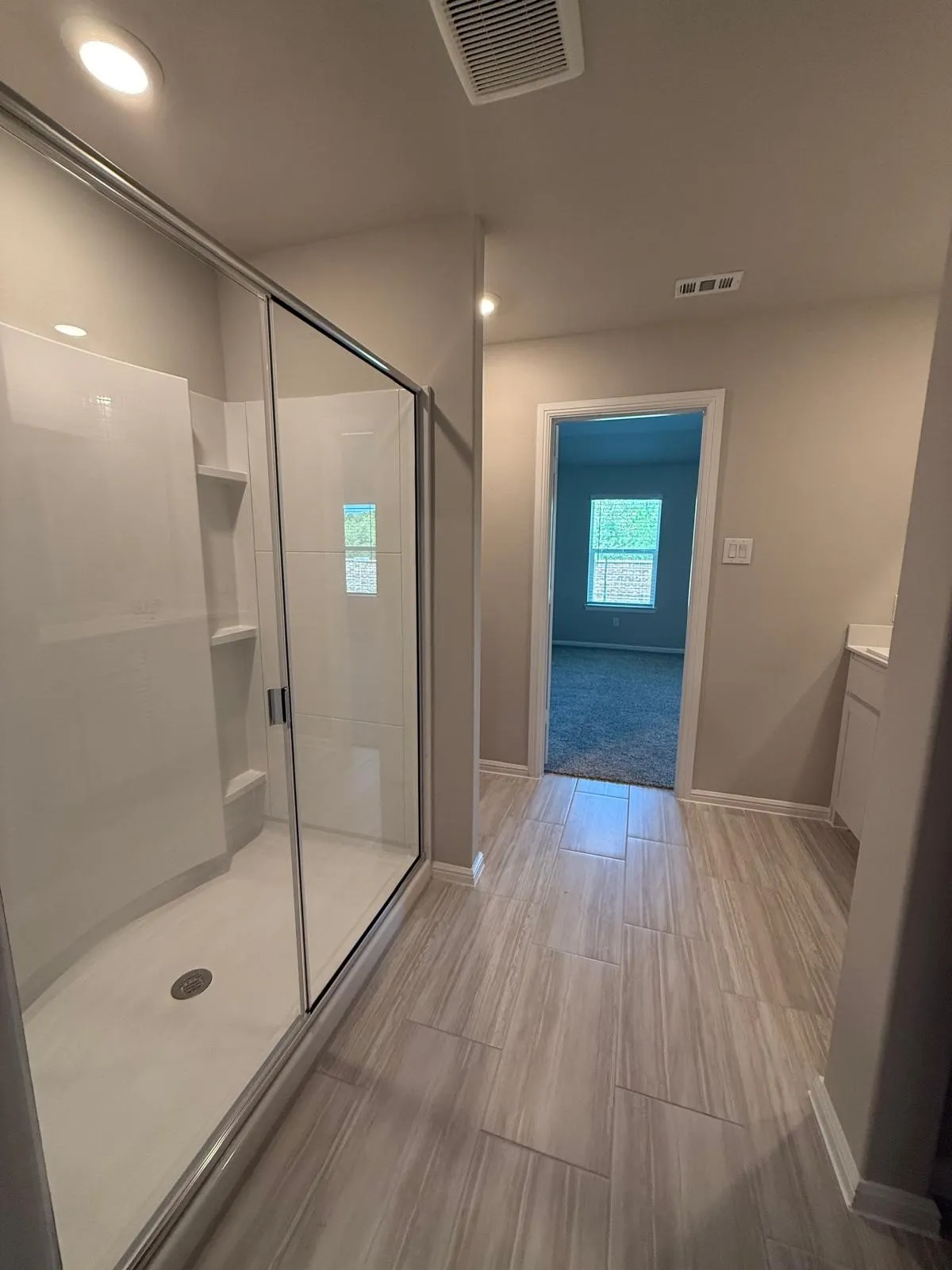 Walk-in shower with a glass enclosure, integrated shelving, and wood-finish tile flooring