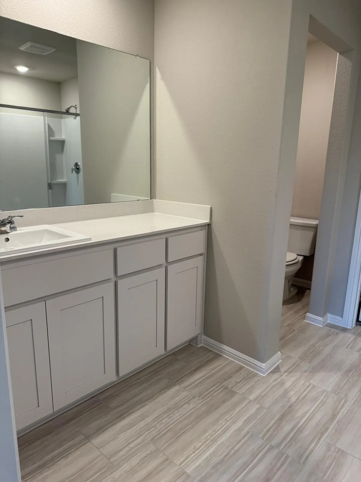 Bathroom featuring a vanity with white cabinetry, a solid-surface countertop with an integrated basin, a large wall-mounted mirror, and wood-finish flooring